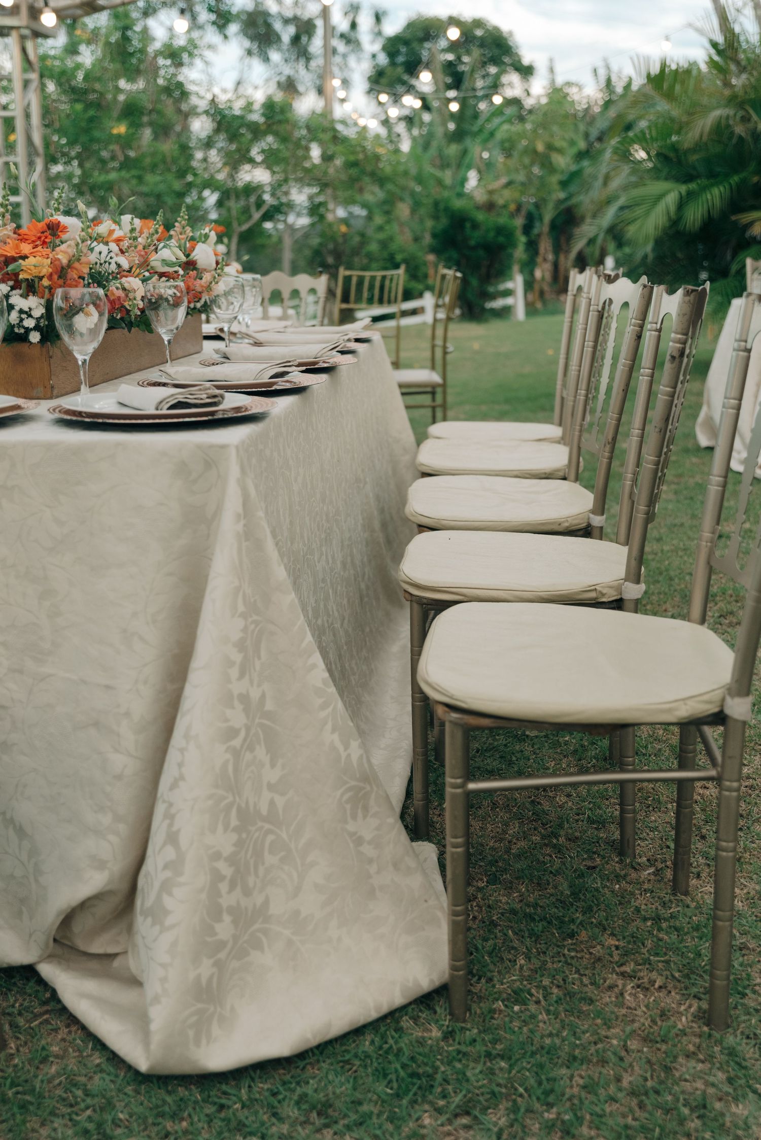 Elegant wedding table setting with cream linens and gold chairs in an outdoor garden.