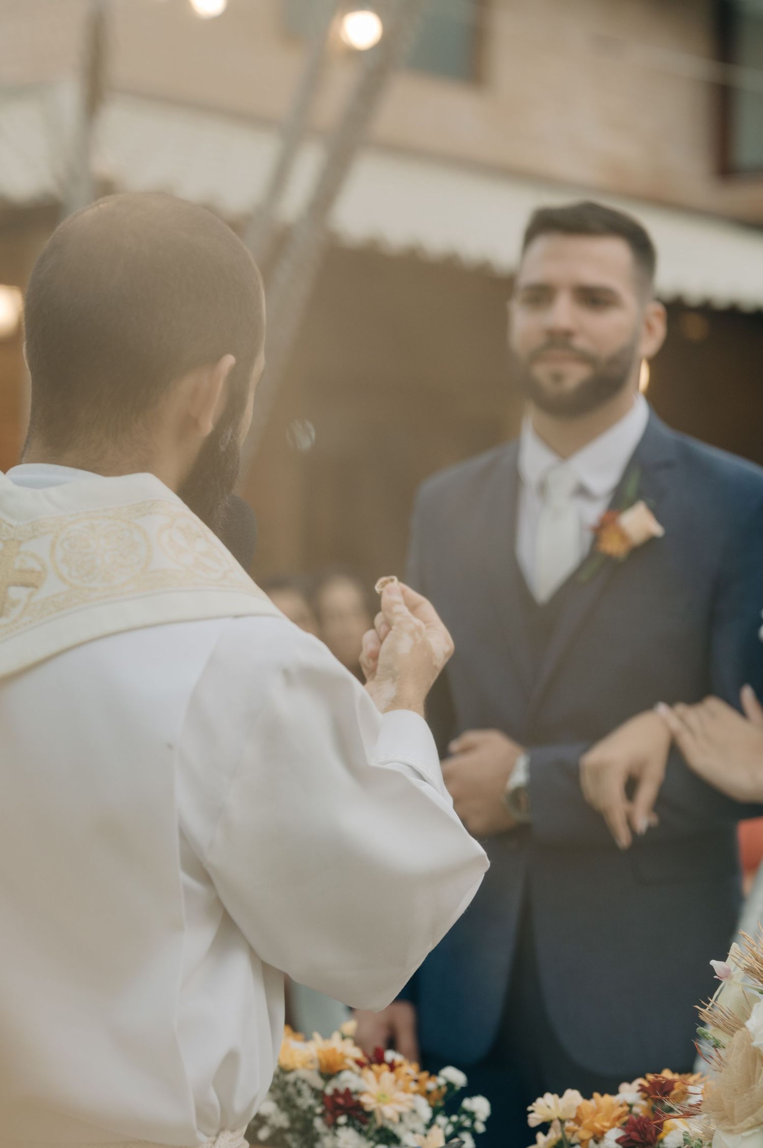 A priest performs wedding ceremony blessings during an outdoor wedding with string lights overhead.