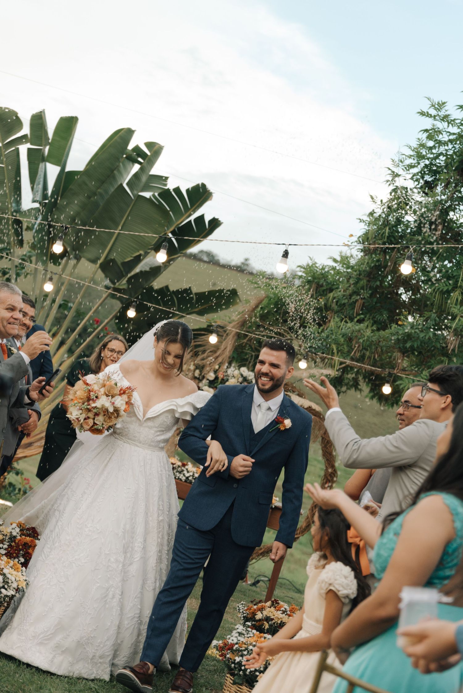 Wedding celebration under string lights and palm leaves as guests celebrate the newly married couple.