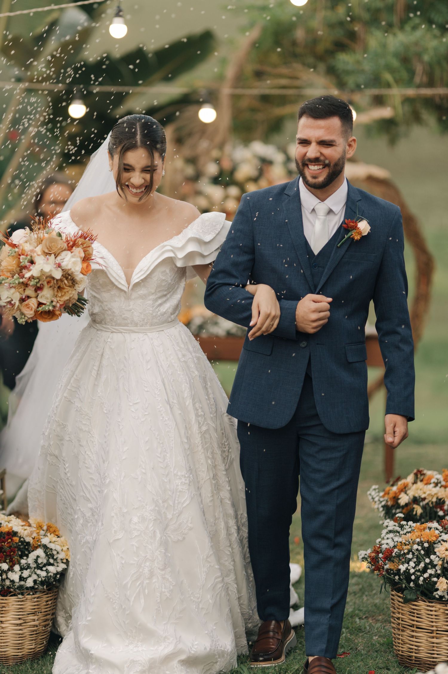 Joyful newlyweds walk down the aisle surrounded by string lights and floral arrangements.