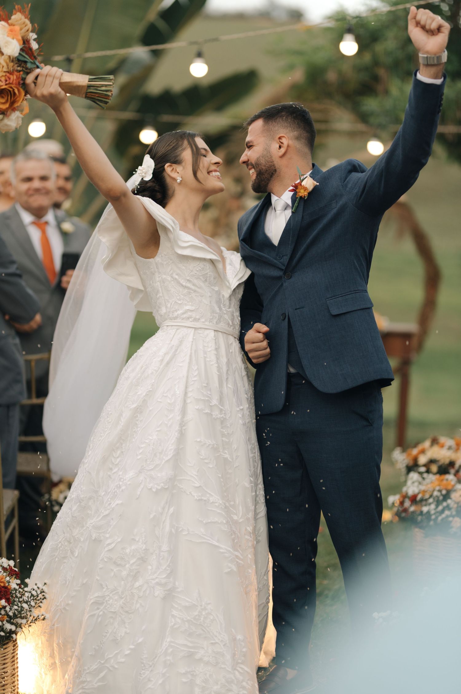 Celebratory moment as newlyweds raise their arms in triumph during outdoor wedding ceremony.