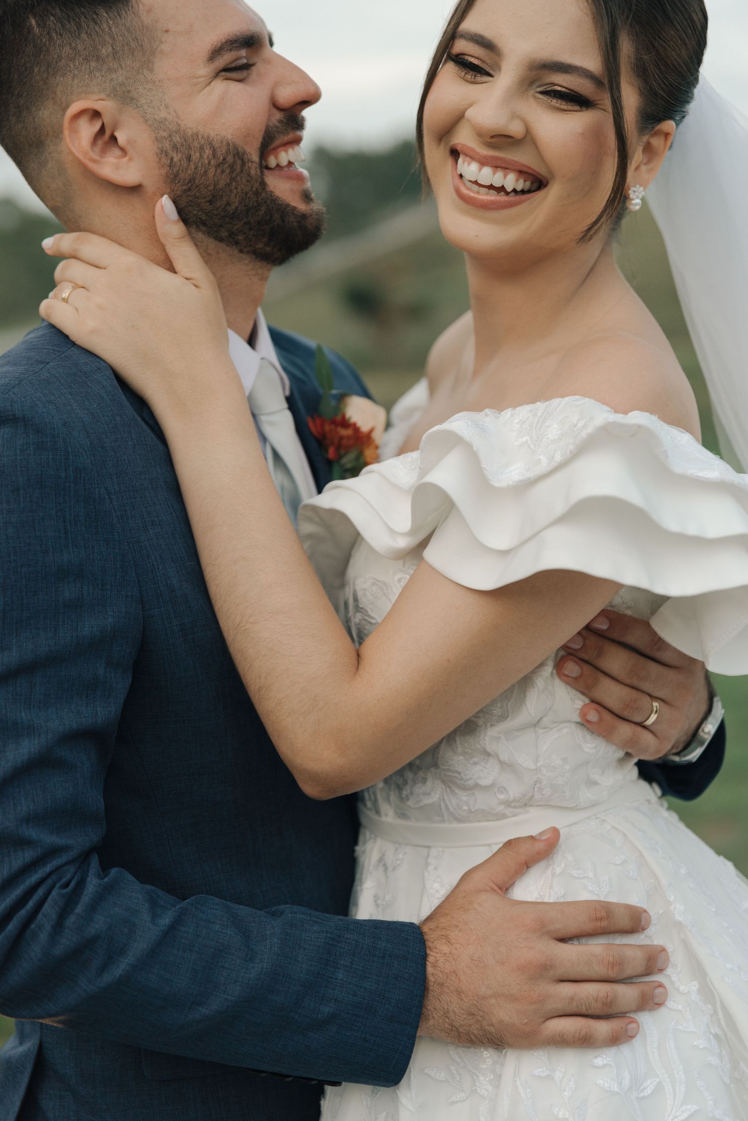 A joyful wedding couple embraces and laughs together, with bride in white dress and groom in navy suit.