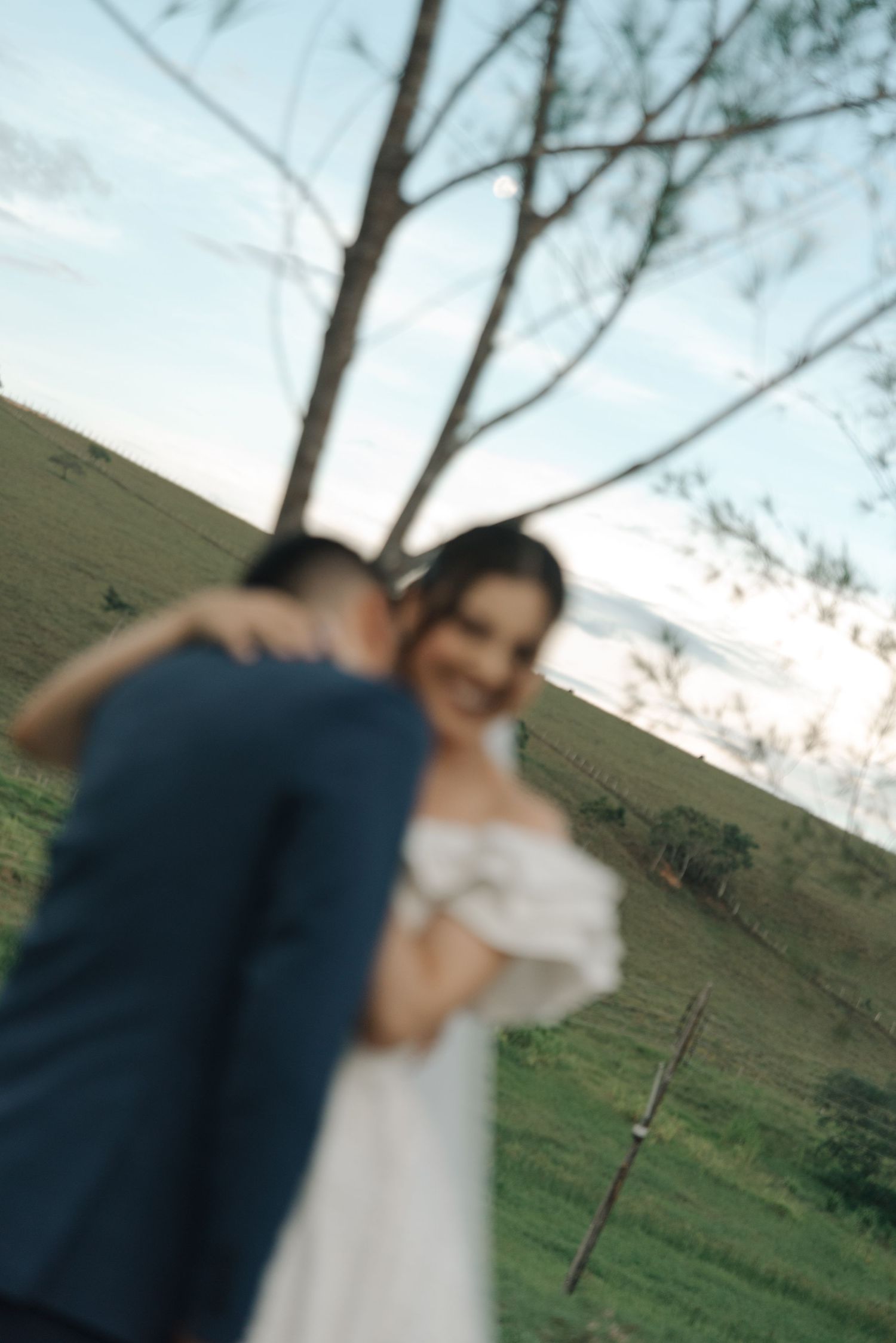 A blurred romantic moment between newlyweds in an outdoor setting with rolling hills.