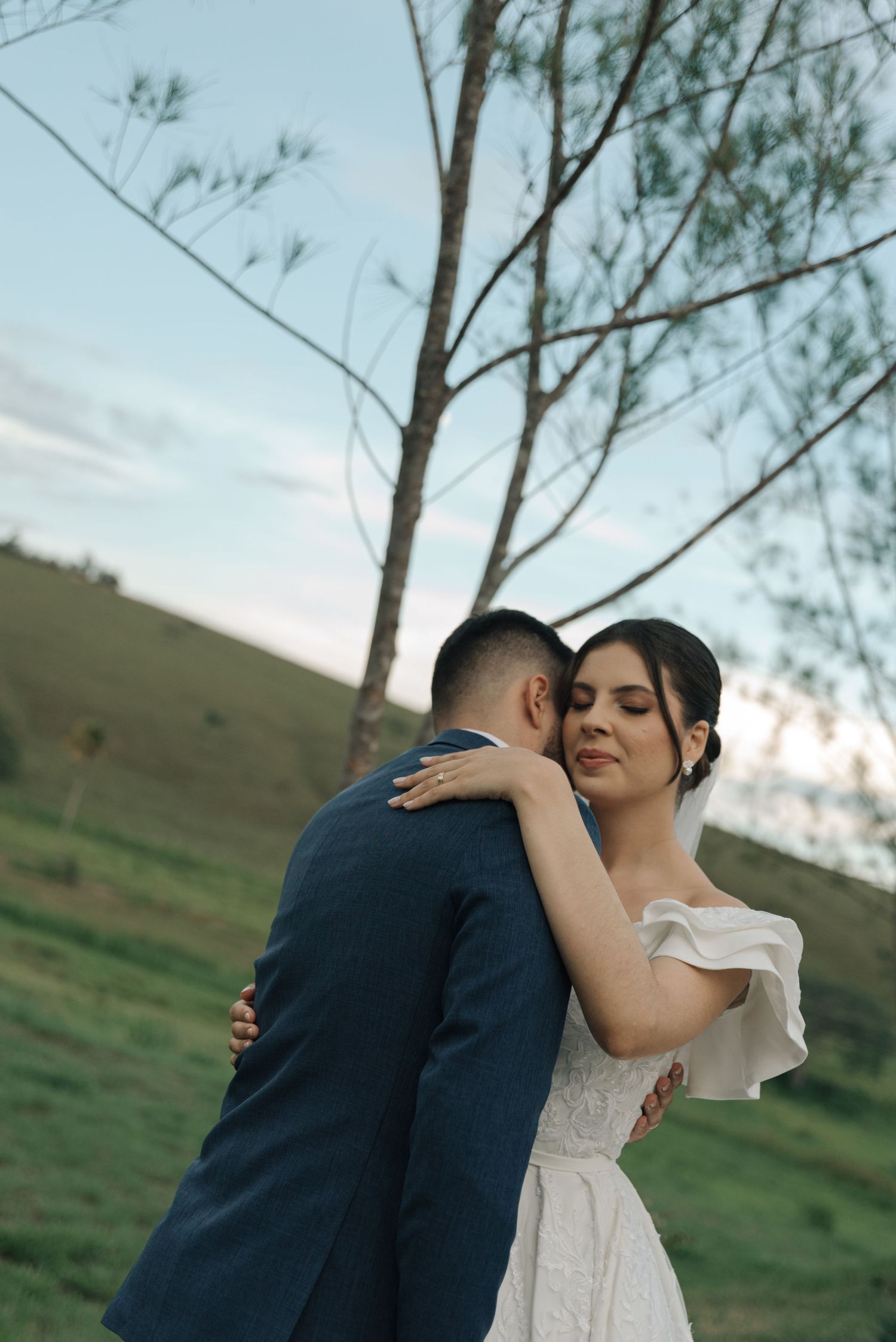 A tender moment between newlyweds against a backdrop of rolling hills and a lone tree.