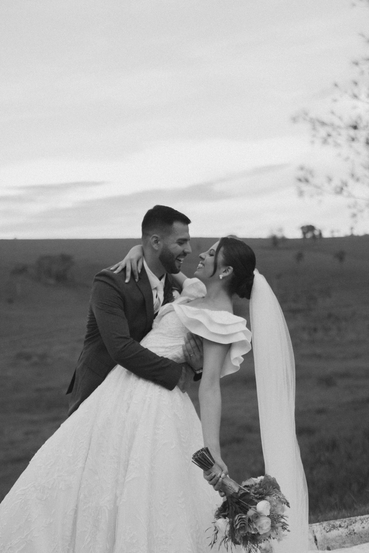 Black and white wedding photo of a romantic dip pose with rolling hills in background.