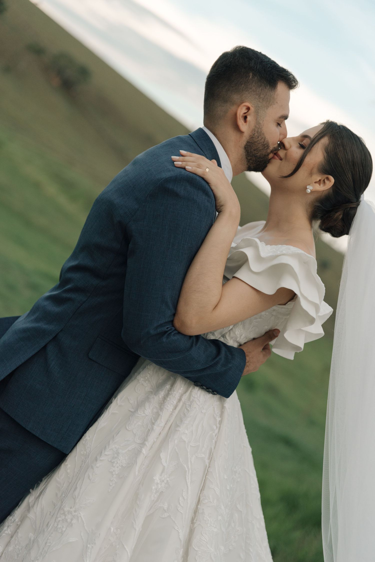 A romantic wedding kiss captured in front of rolling hills with bride in classic white gown.