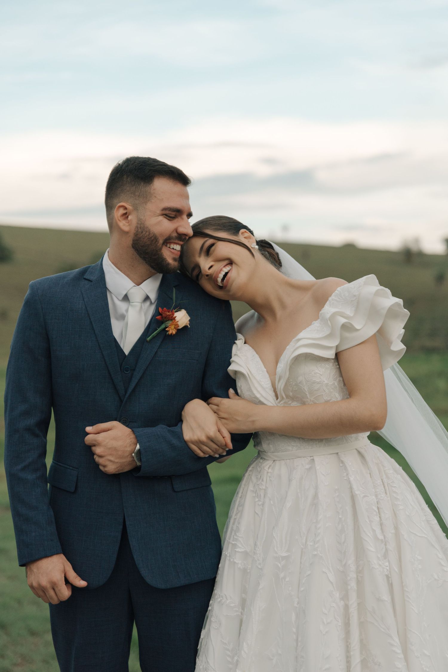 Joyful newlyweds share a candid laughing moment together in an outdoor countryside setting.