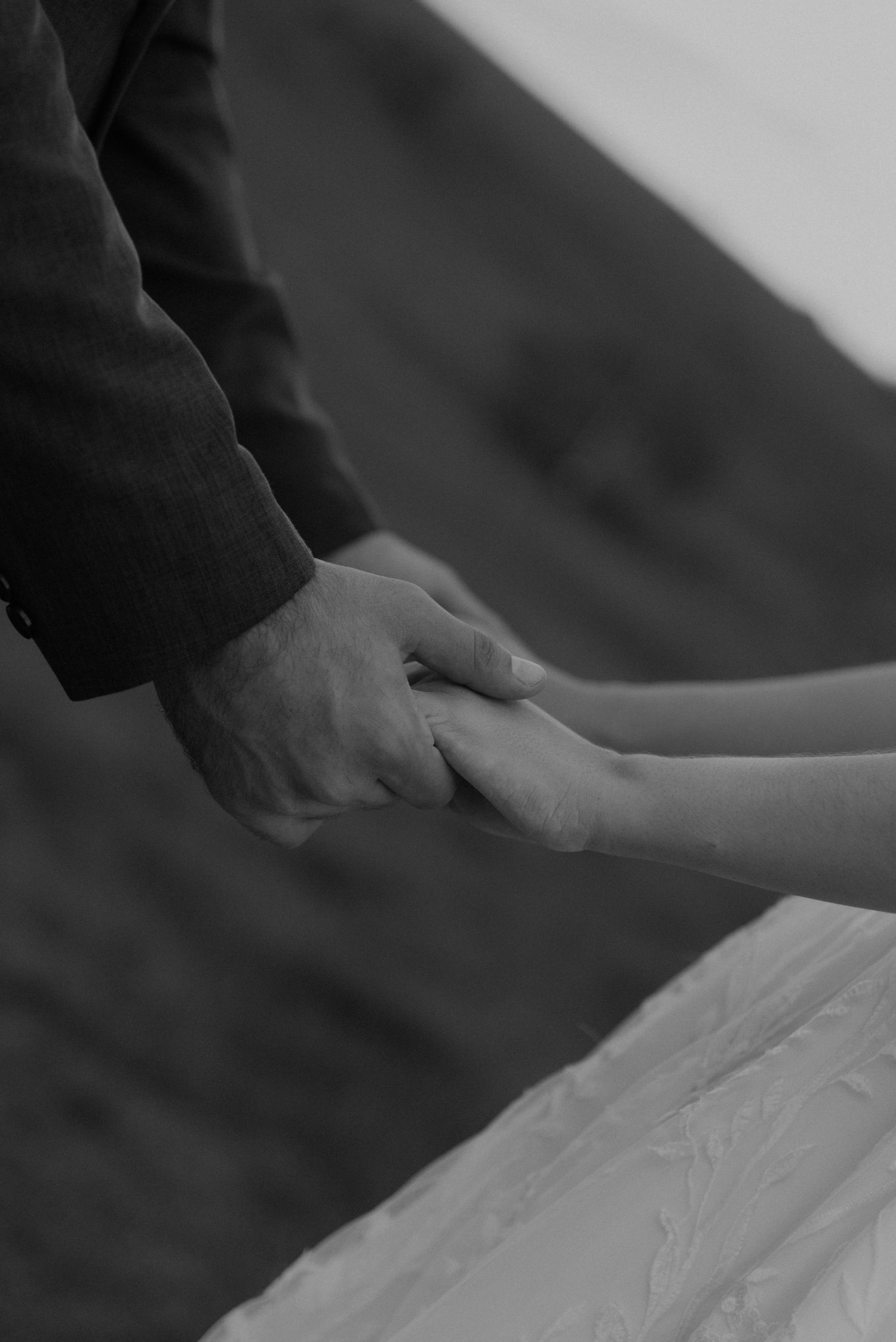 Black and white image capturing hands tenderly clasped together during a wedding ceremony.