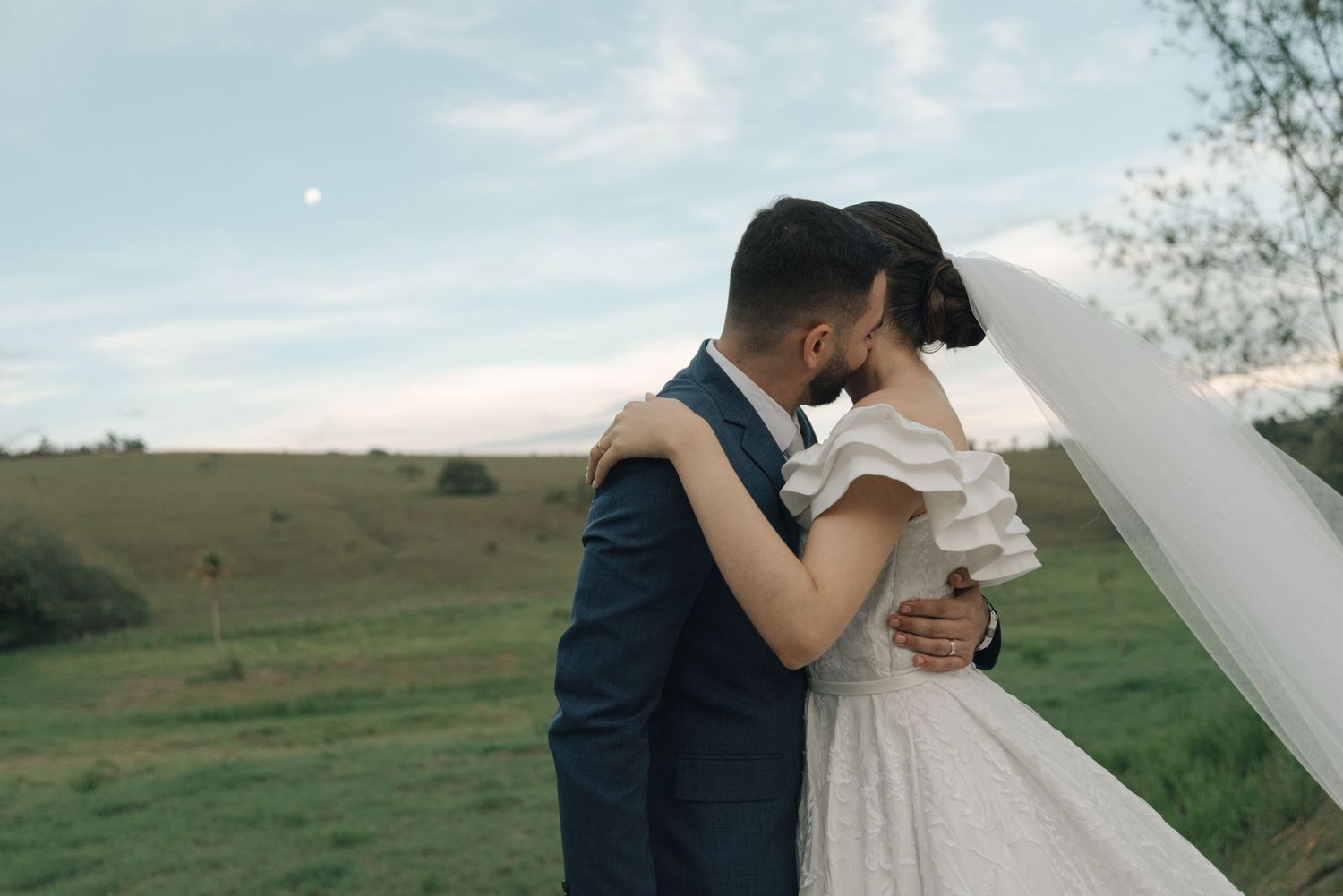 Newlyweds share an intimate moment in an outdoor setting with rolling hills in the background.