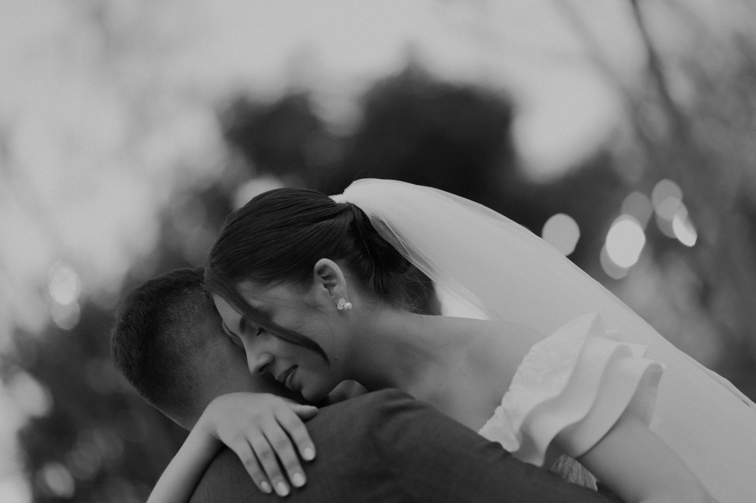 Black and white candid photo captures newlyweds in a joyful embrace during their wedding.