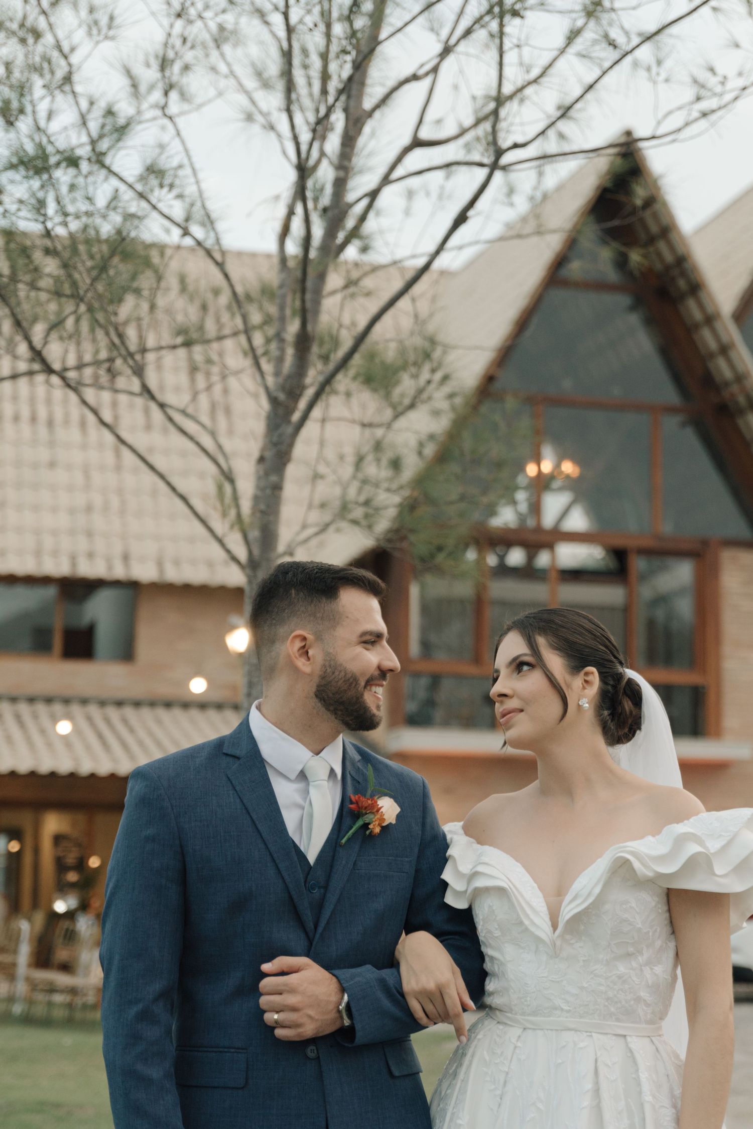 A romantic outdoor wedding scene with a couple in formal attire against an A-frame chapel backdrop.
