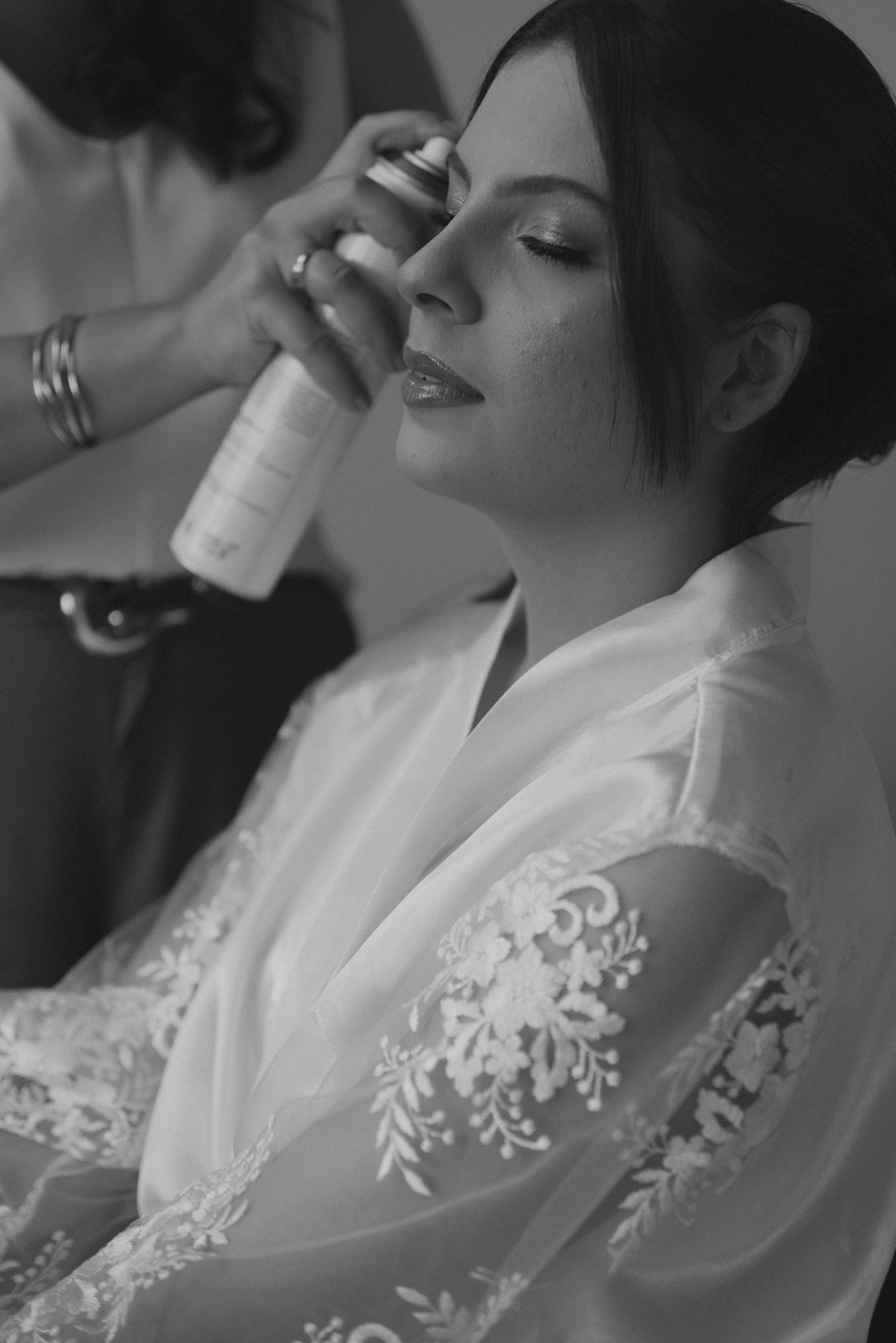 Elegant black and white photo of bridal makeup application in lace robe.