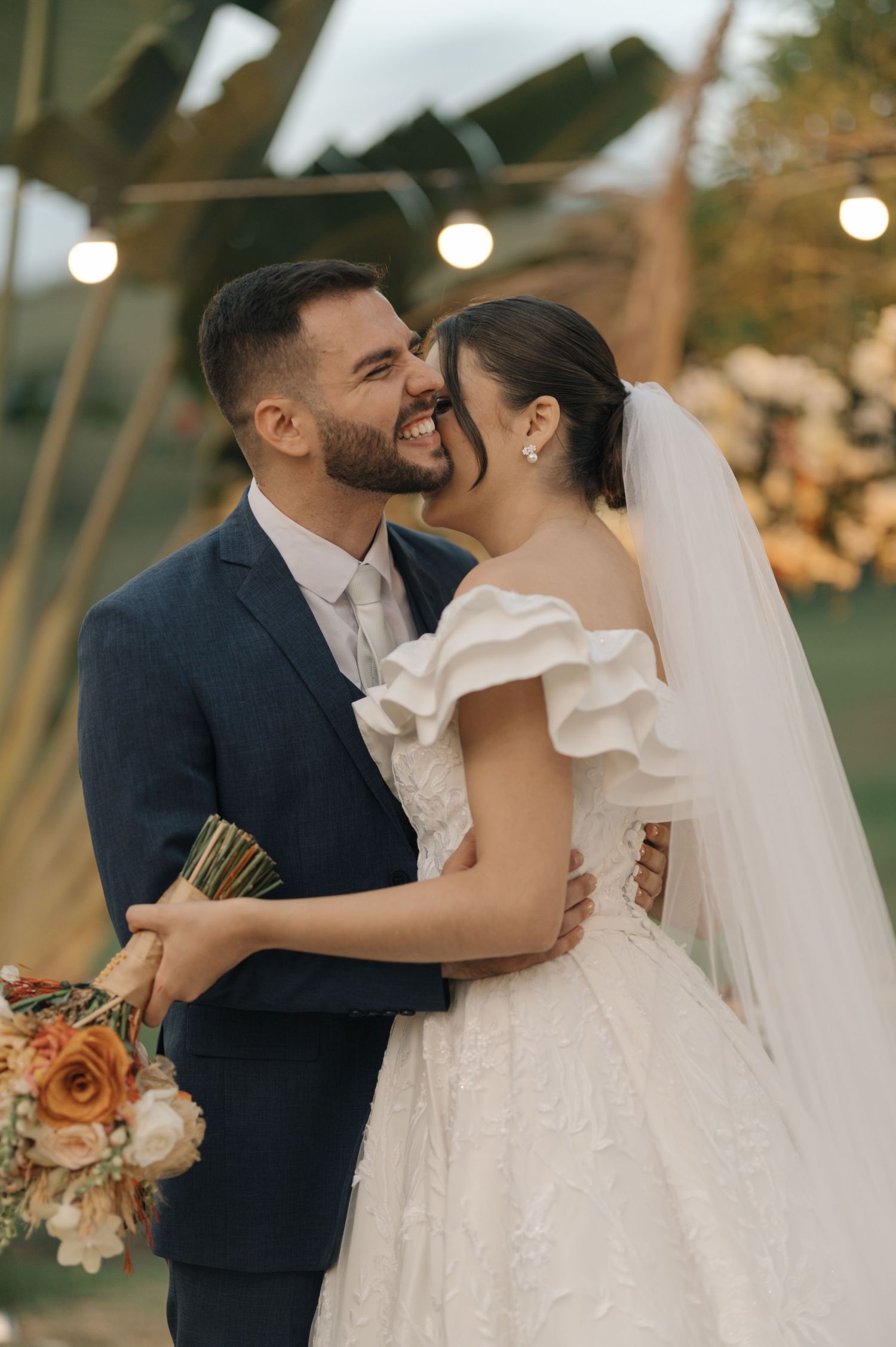 A joyful wedding moment captured outdoors with tropical plants and warm lighting.