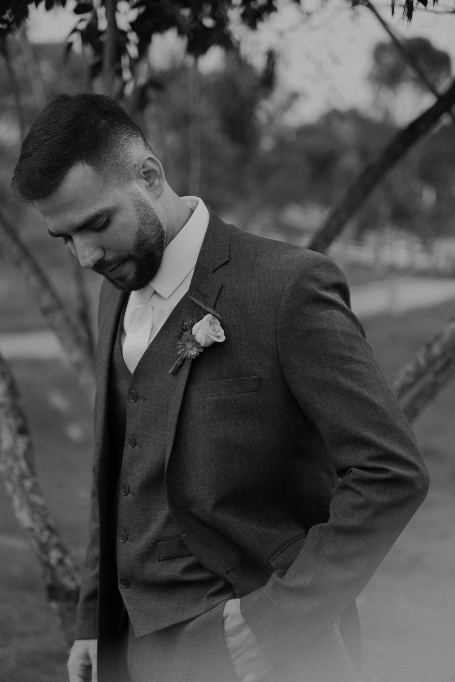 A black and white portrait of a groom in a three-piece suit with a boutonniere.