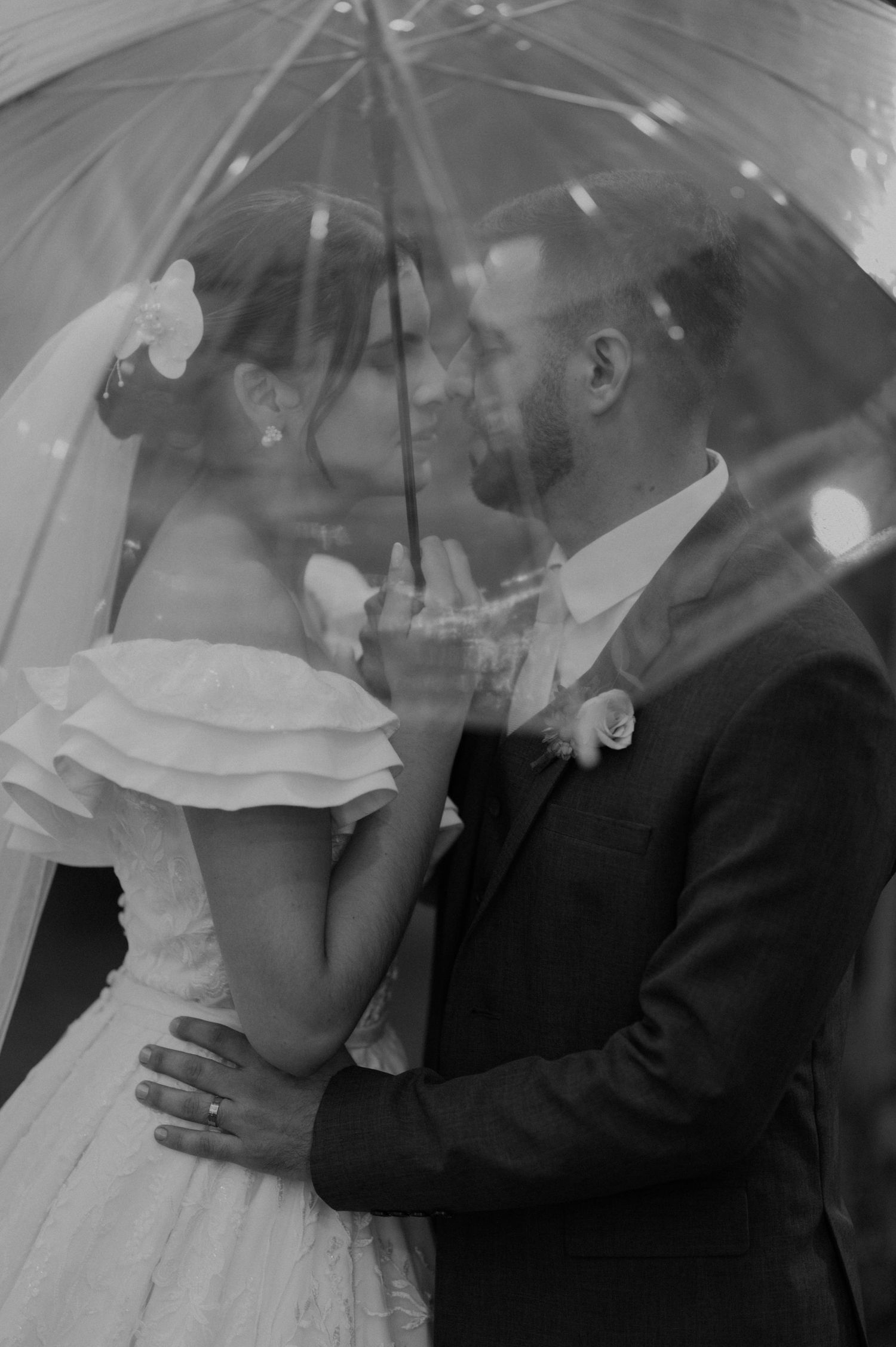 A romantic black and white photo of newlyweds sharing an intimate moment under an umbrella.