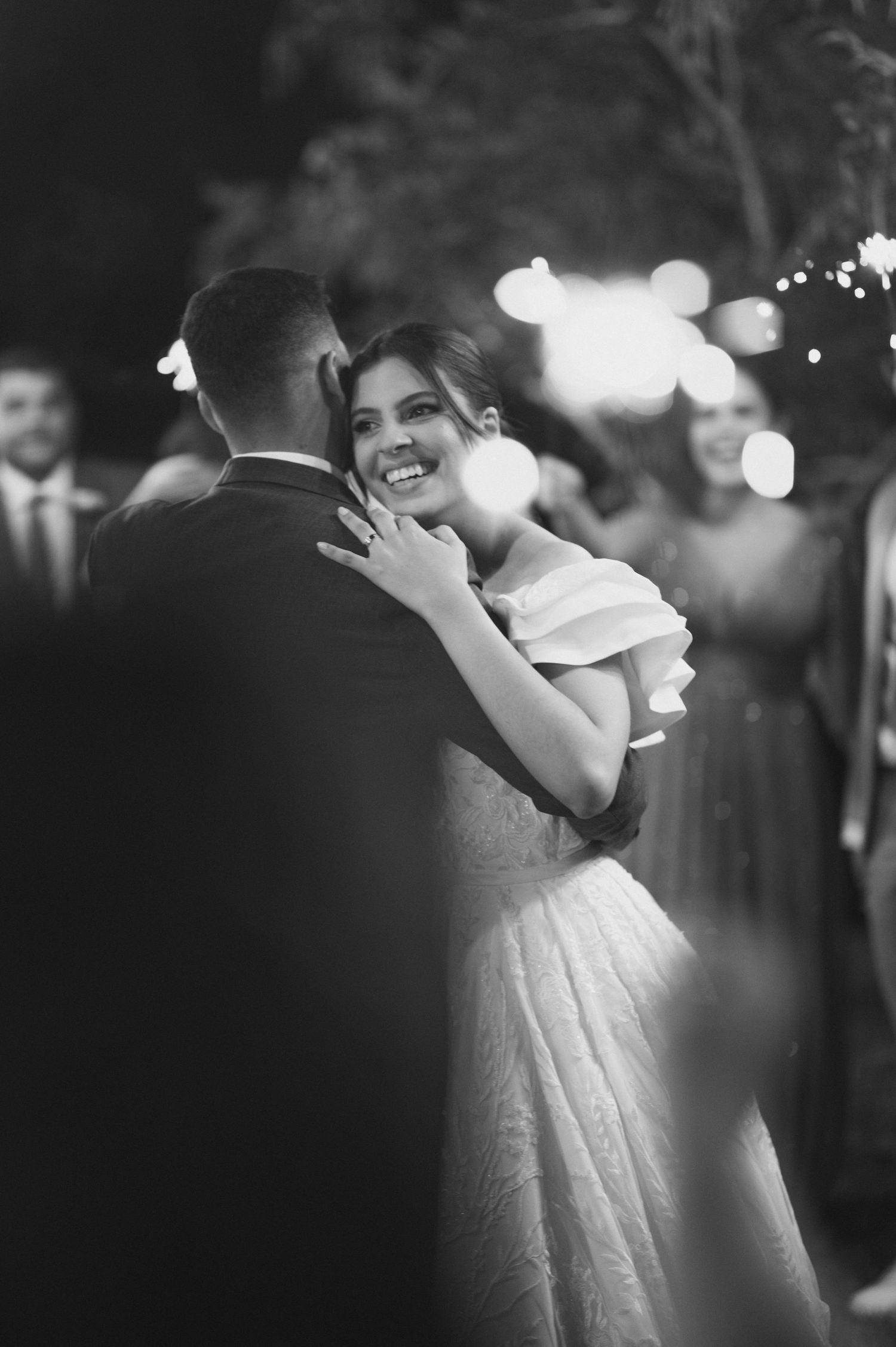 A romantic black and white wedding dance moment as a couple embraces under twinkling lights.