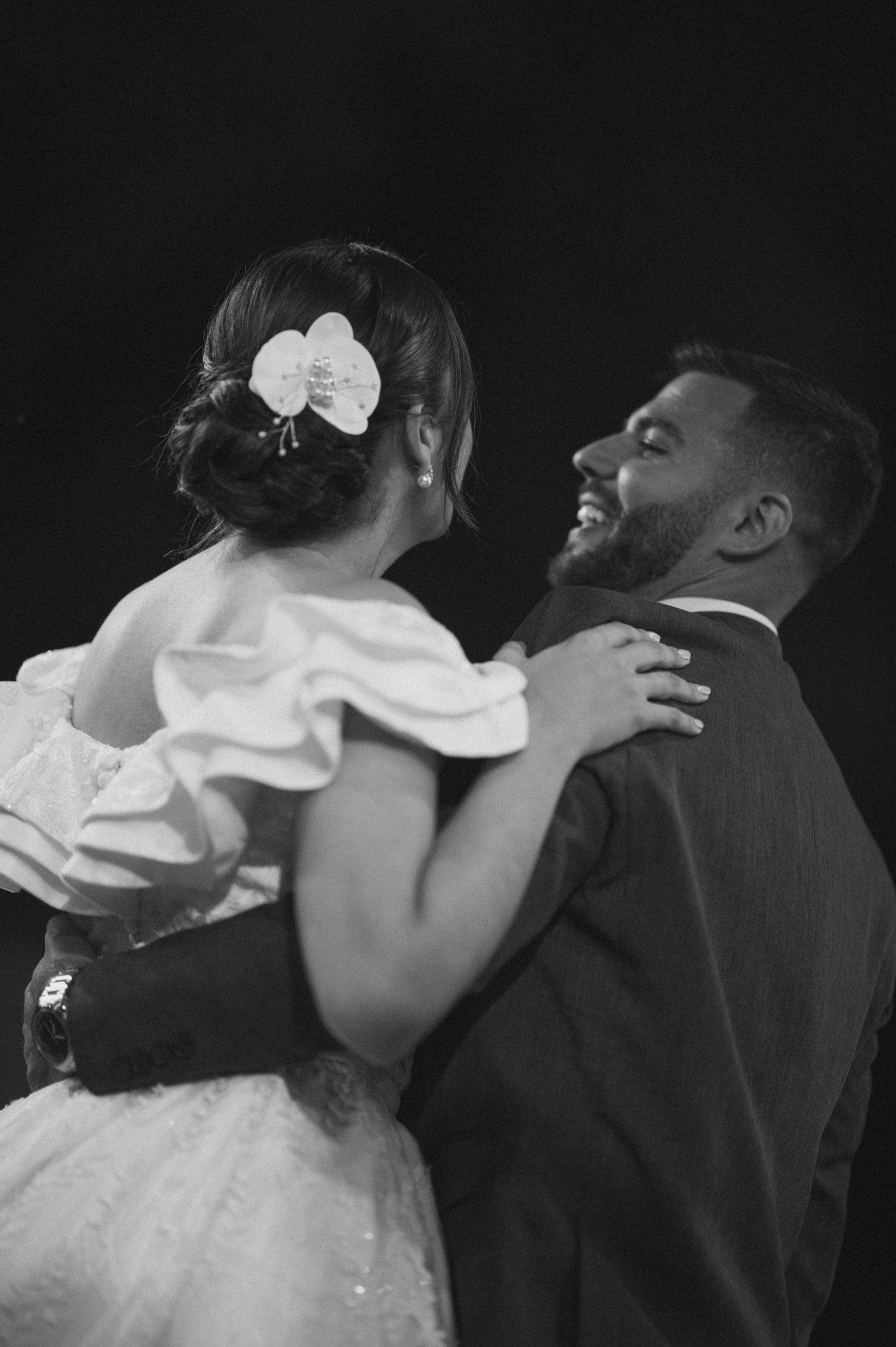 A joyful wedding dance captured in black and white with the bride wearing an orchid hair accessory.