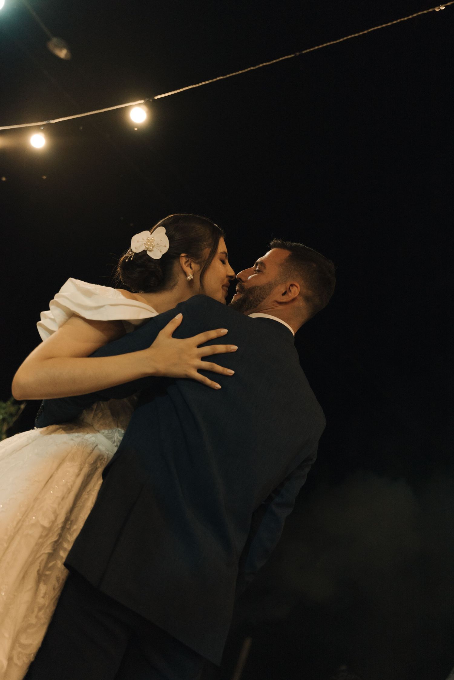 Newlyweds sharing an intimate moment under string lights during their outdoor reception.