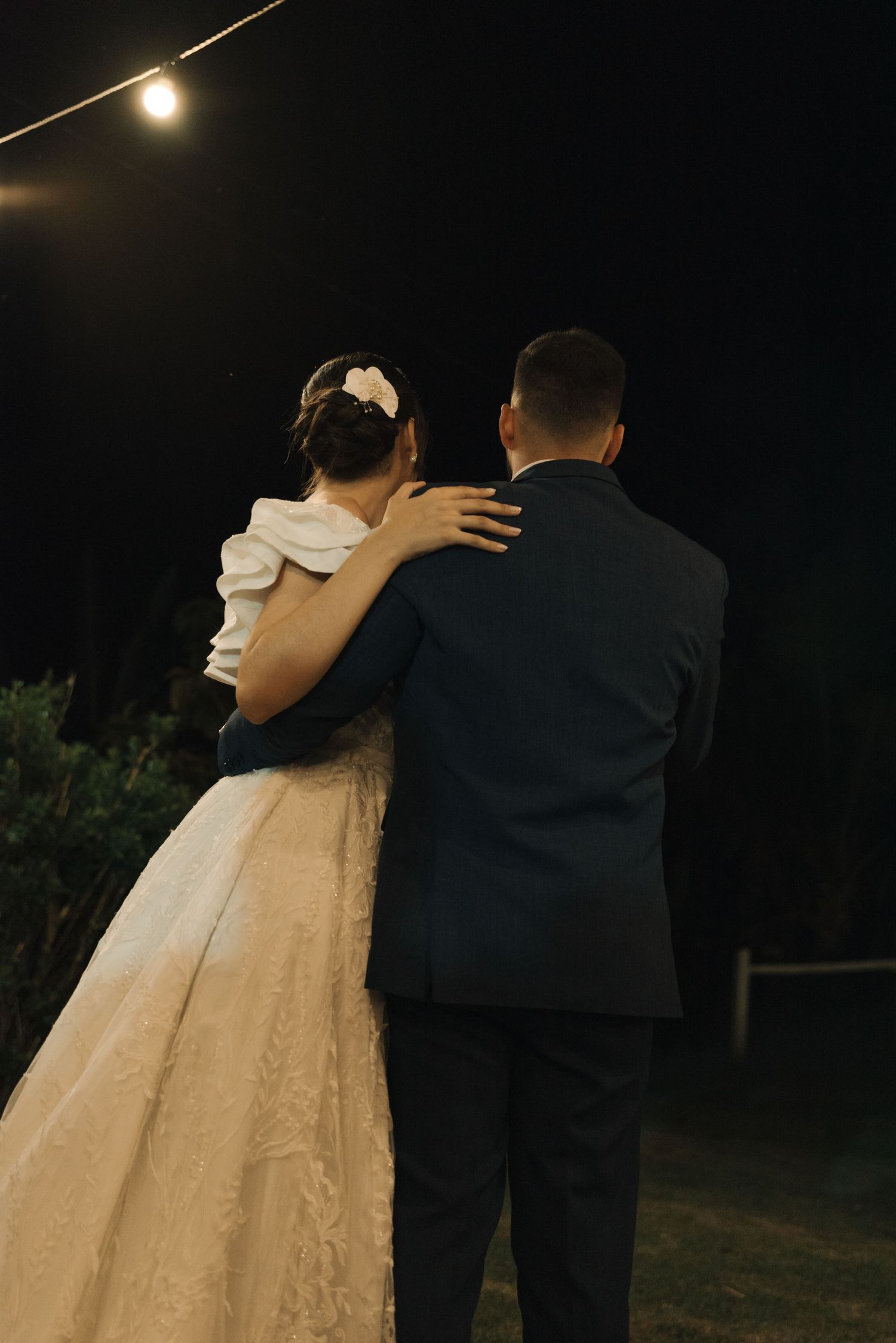 A tender moment between newlyweds under outdoor lighting at dusk.