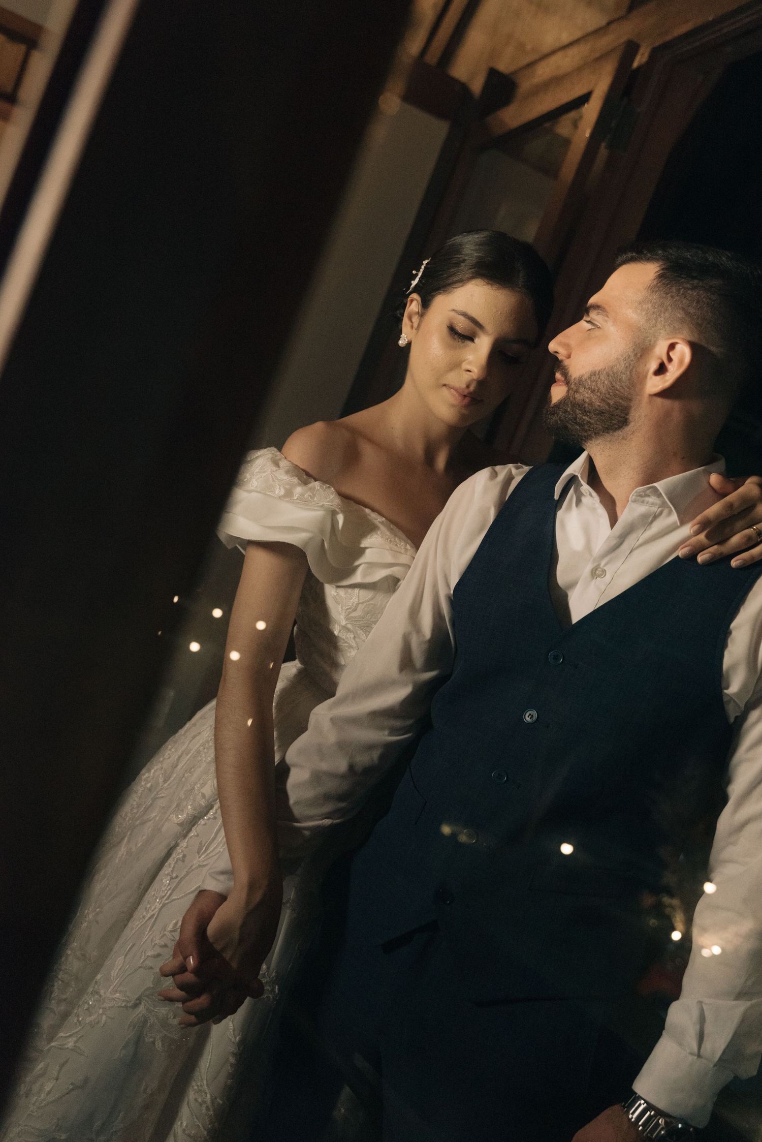 A romantic indoor portrait of newlyweds with soft fairy lights in the background.