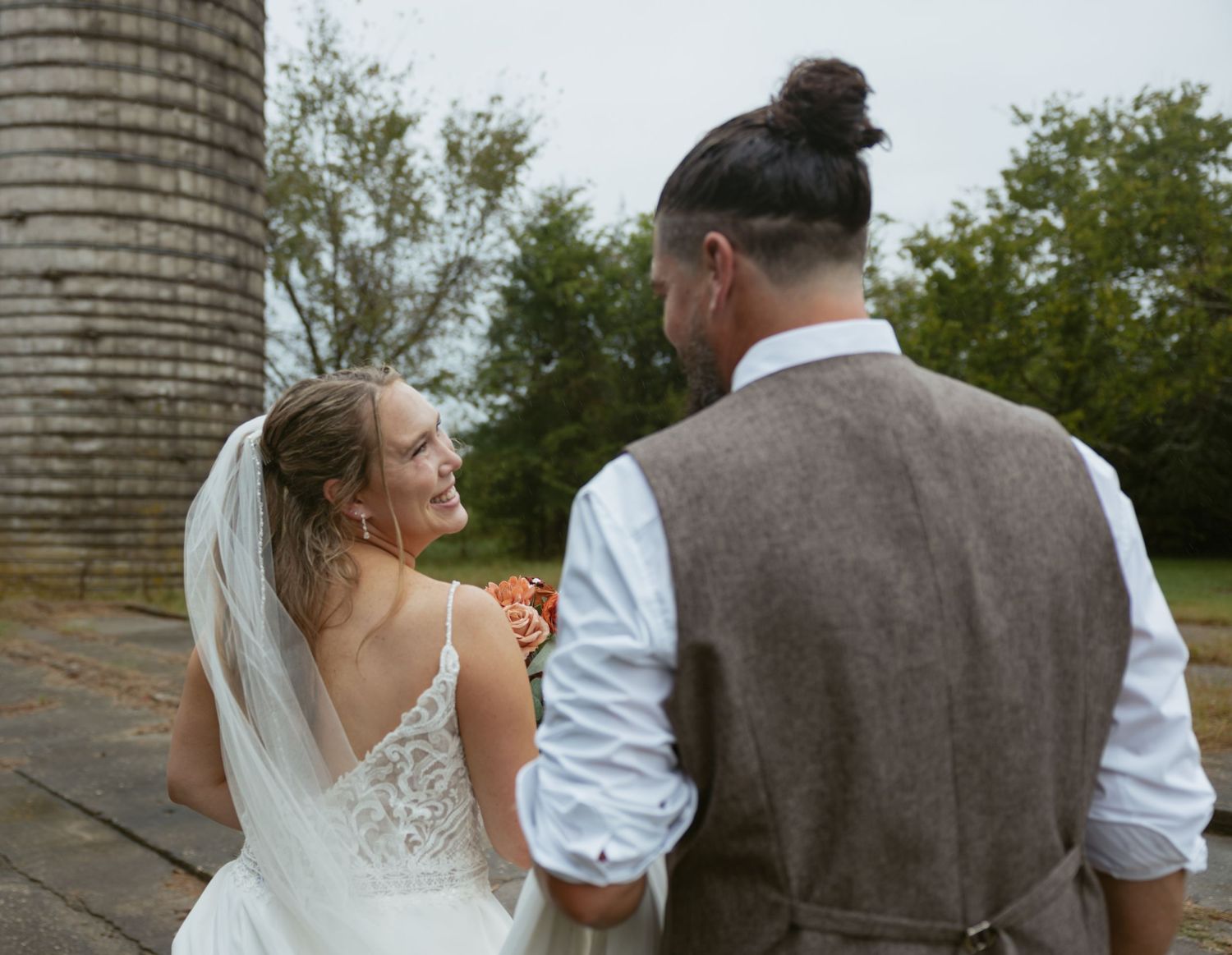 A couple in wedding attire share a moment together near a rustic silo on their special day.