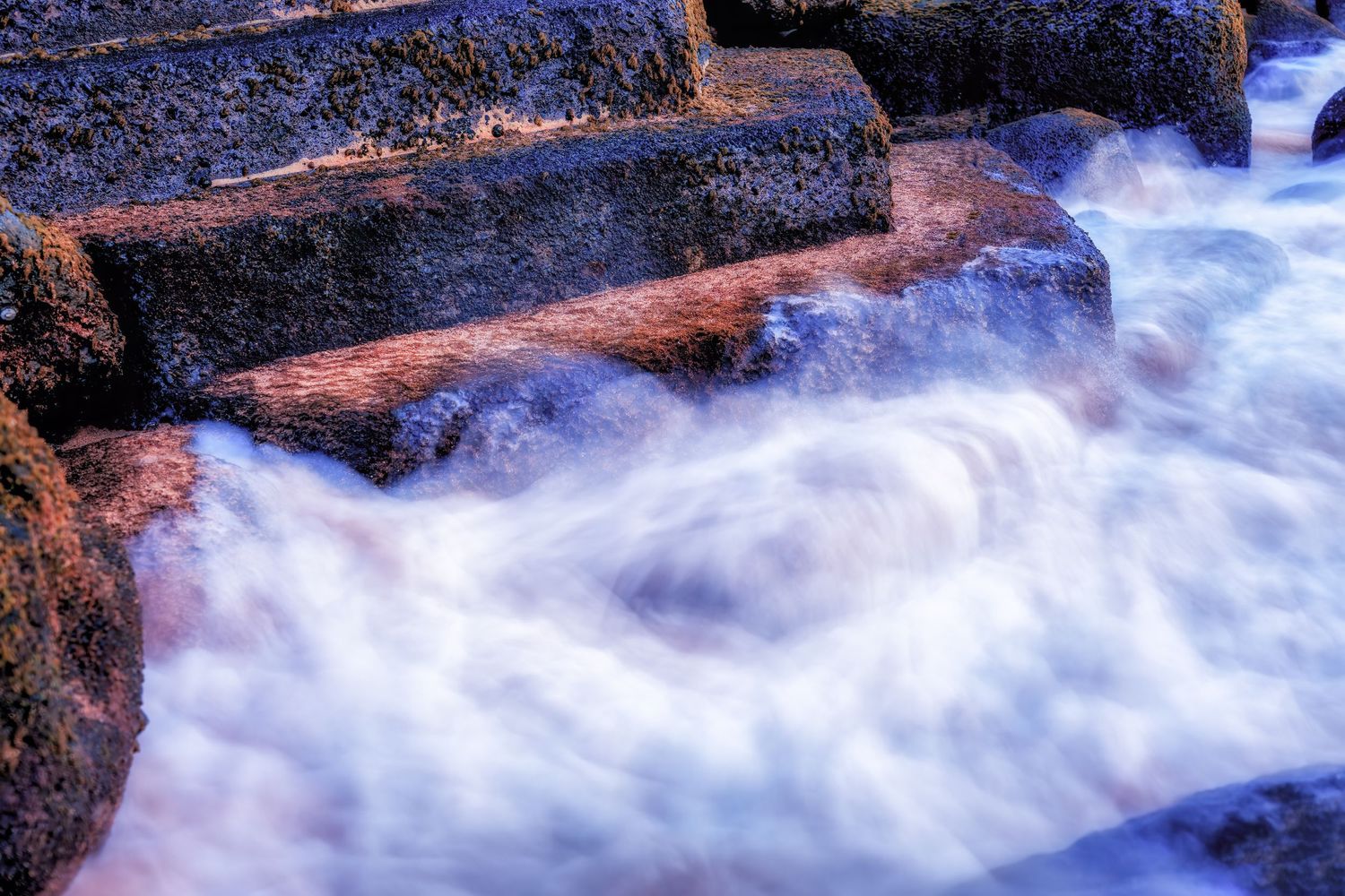 Fast-flowing water cascades over rocky steps creating a misty ethereal effect in long exposure photography.