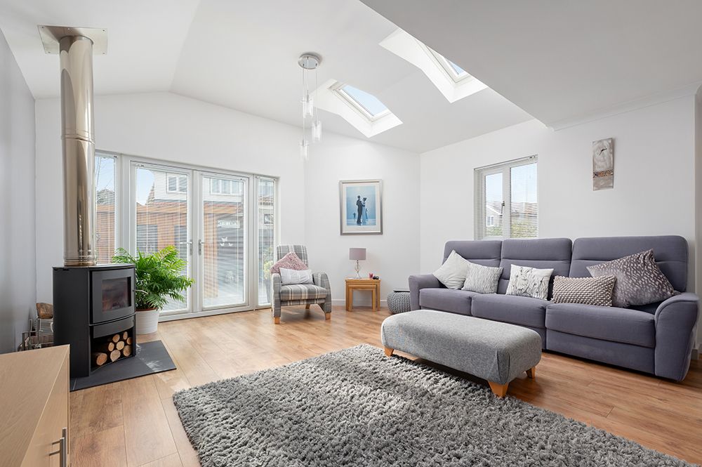 Modern living room with skylights, gray sectional sofa, wood stove, and French doors leading to outdoor patio.