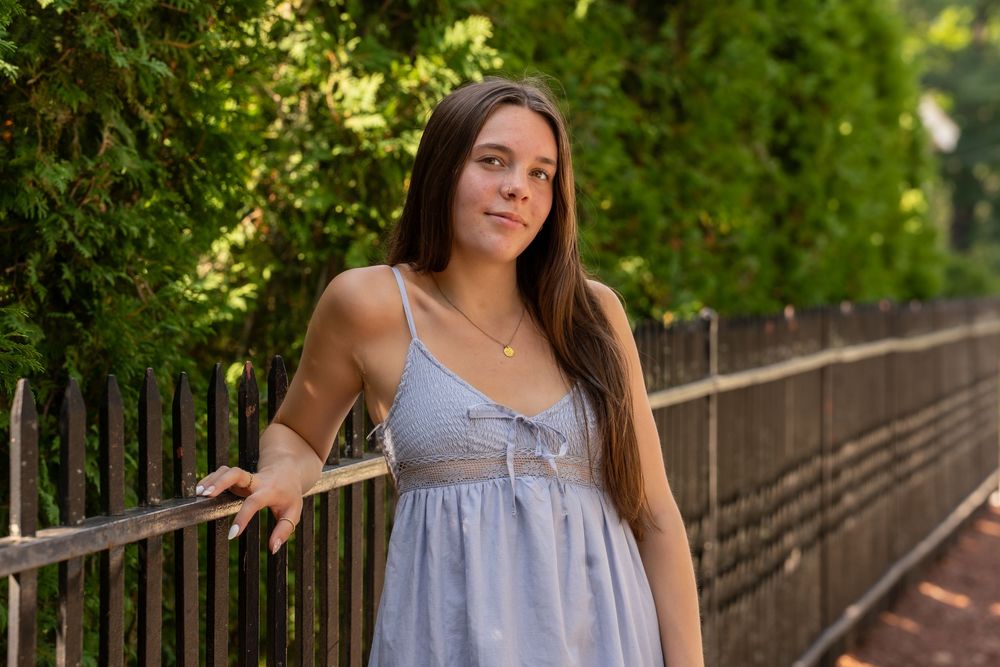 Person in gray summer dress leaning against railing on wooden bridge surrounded by greenery.