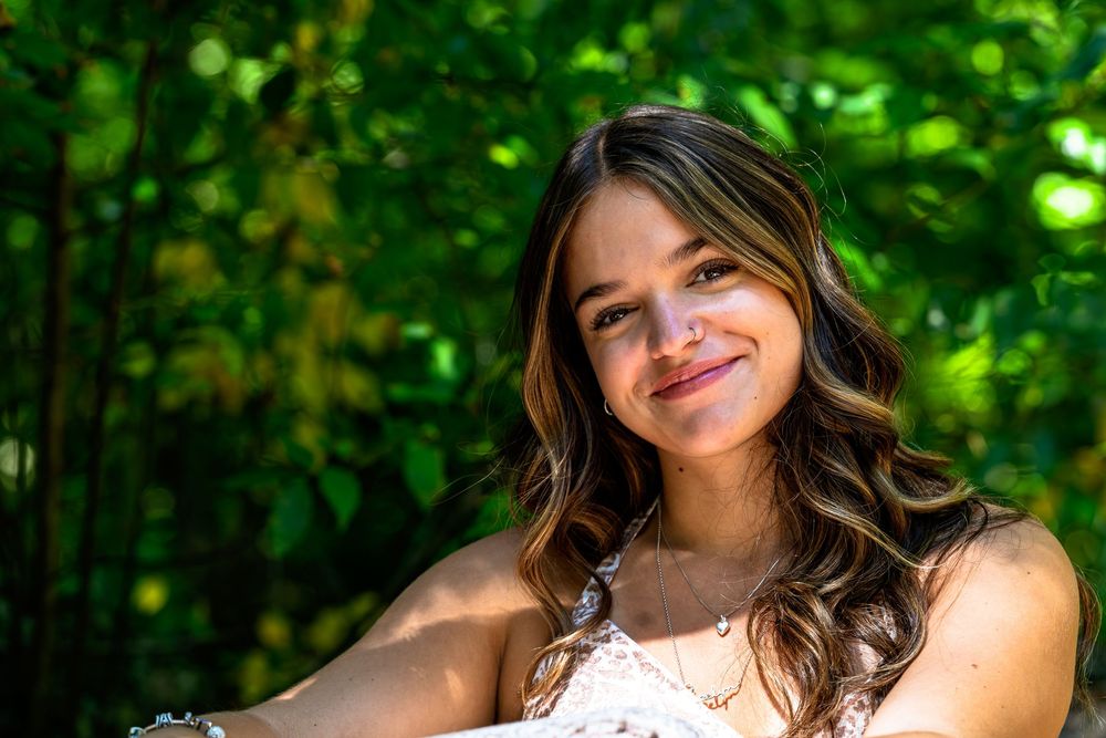 Person smiling in sunlit forest wearing white lace dress.