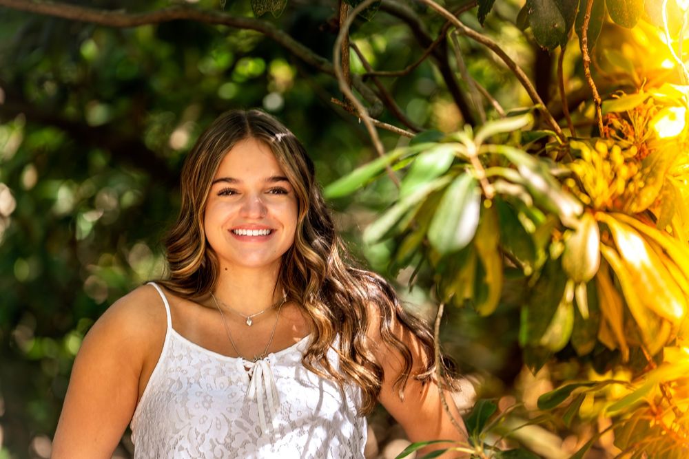 Person in white dress standing in garden with golden sunlight filtering through leaves.