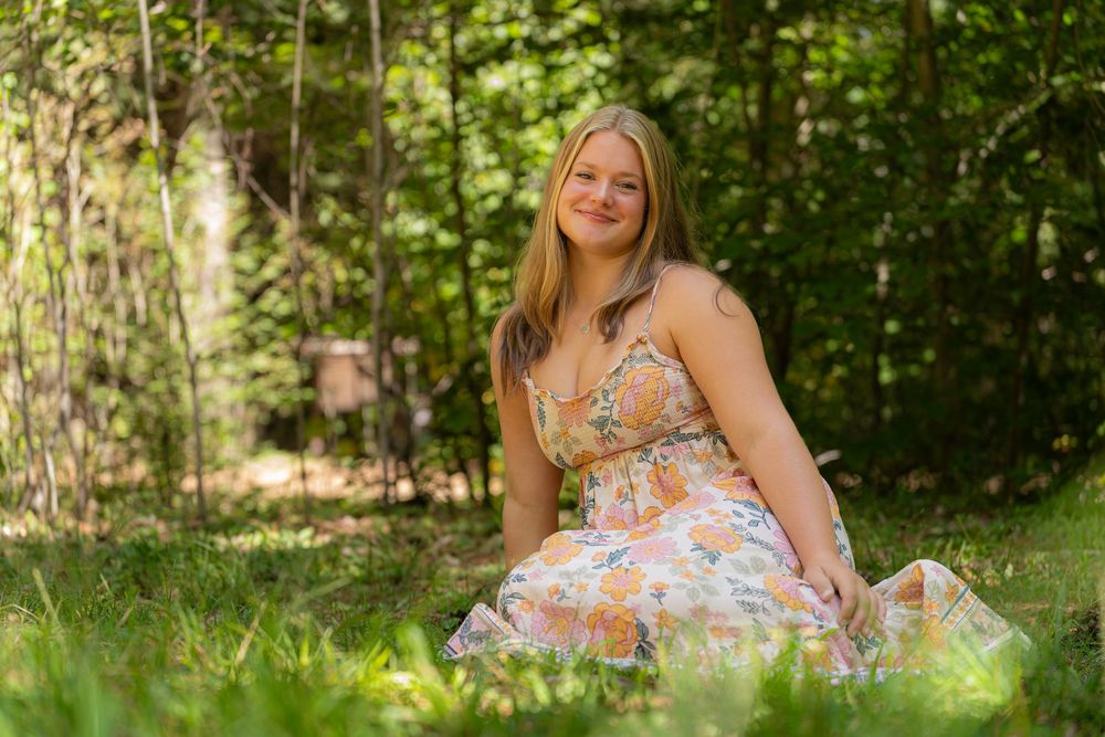Person in floral dress sitting on grass in sunlit garden setting.