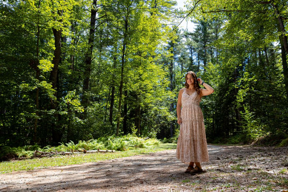 Person in flowy dress twirling on forest path surrounded by tall green trees.