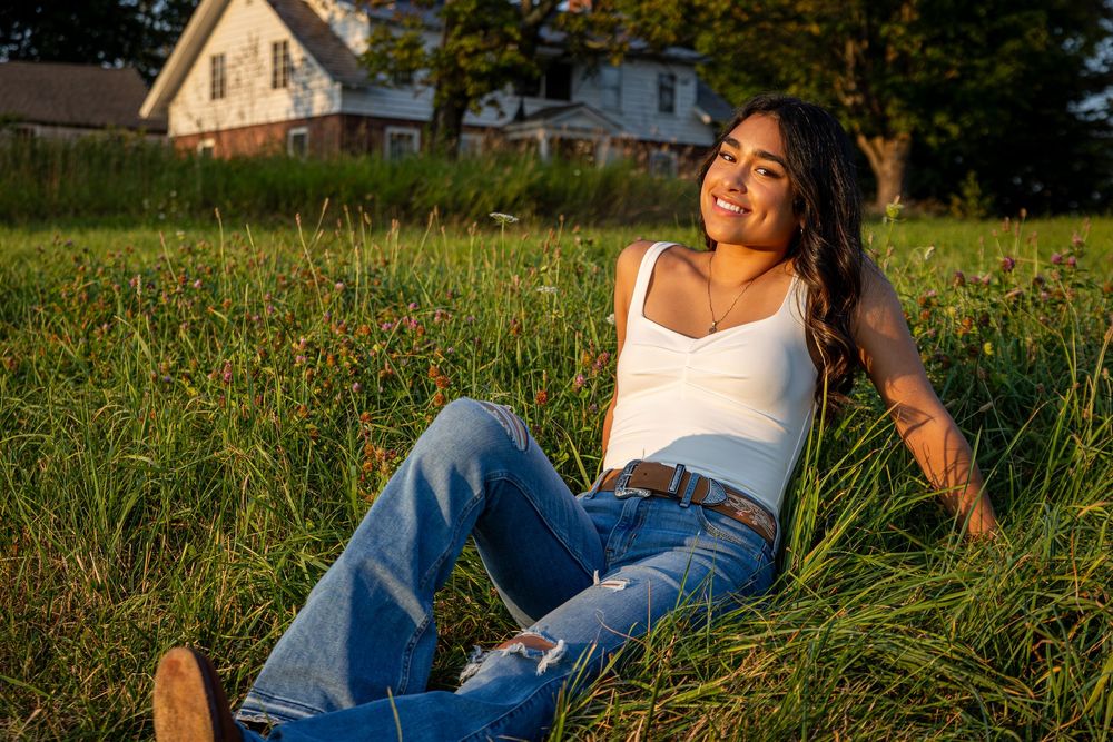Woman in jeans and white top lounging in a sunlit meadow with wildflowers at golden hour.