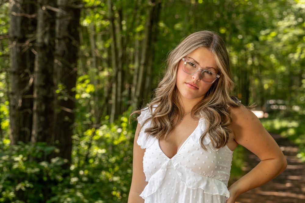Outdoor portrait session in a white summer dress surrounded by green foliage.