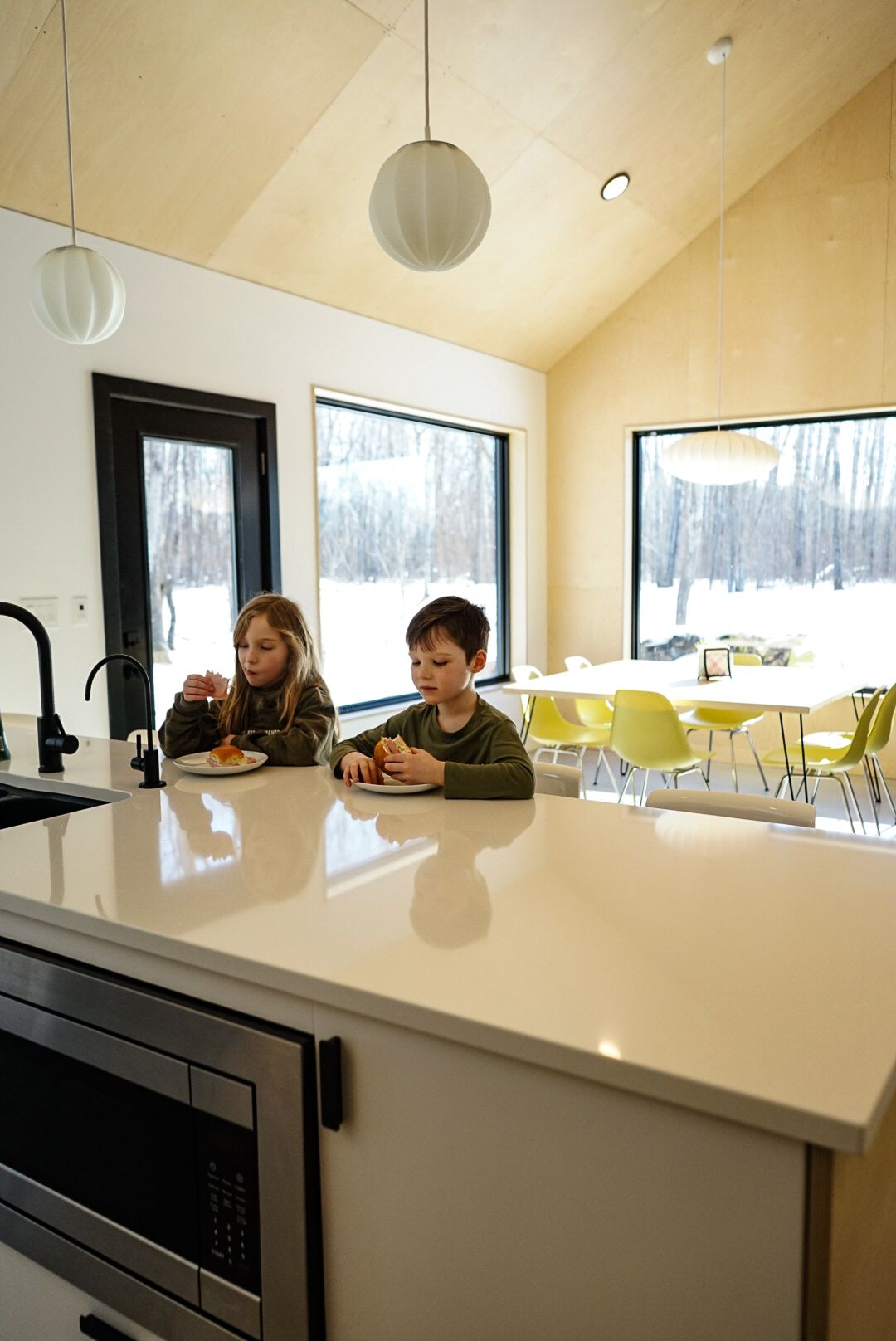 Modern dining area with white counter and yellow chairs overlooking snowy landscape.