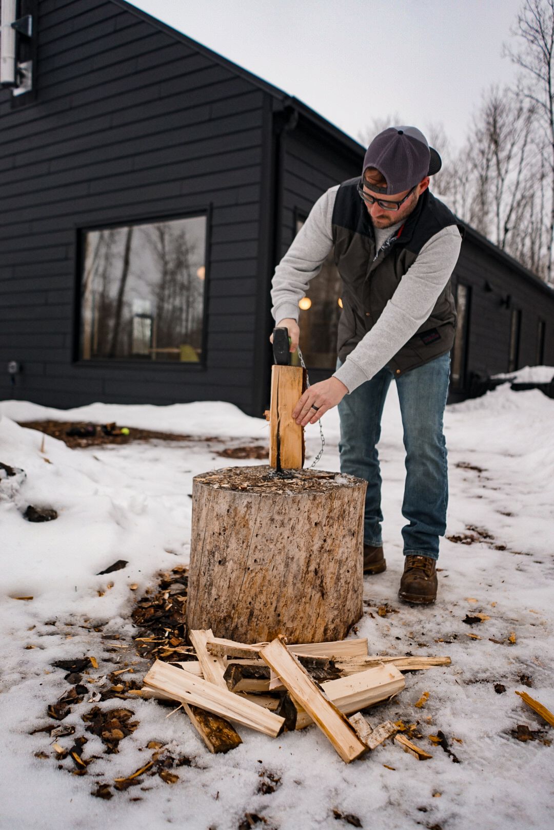 Someone chopping firewood on a snow-covered ground with a large log as a splitting block.