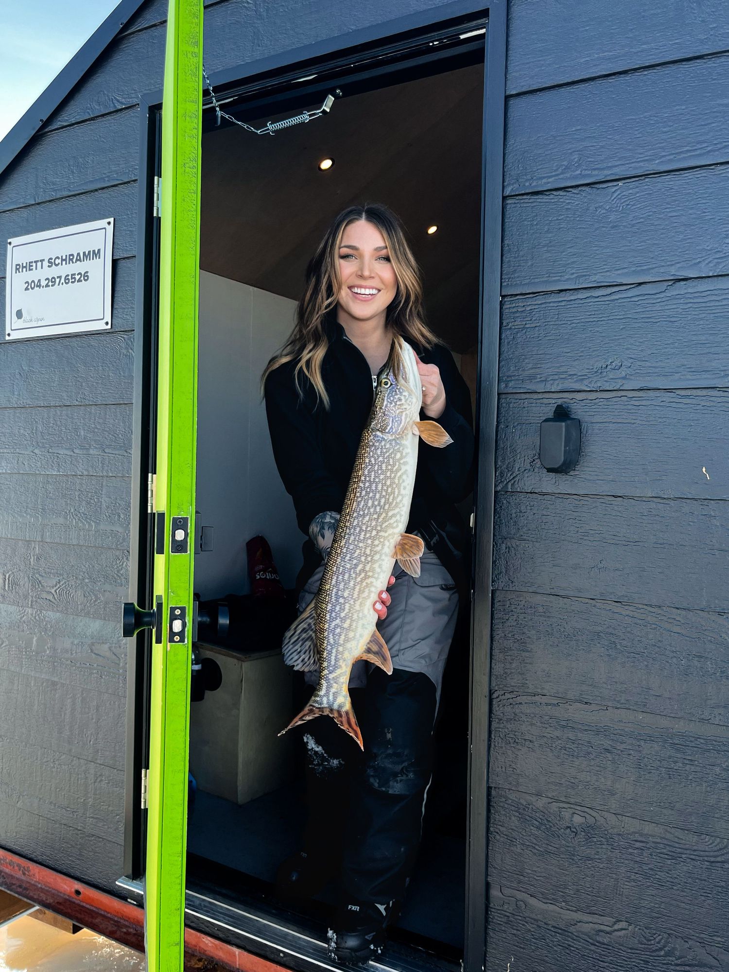 Person holding a large freshly caught fish outside a blue building with lime green door trim.