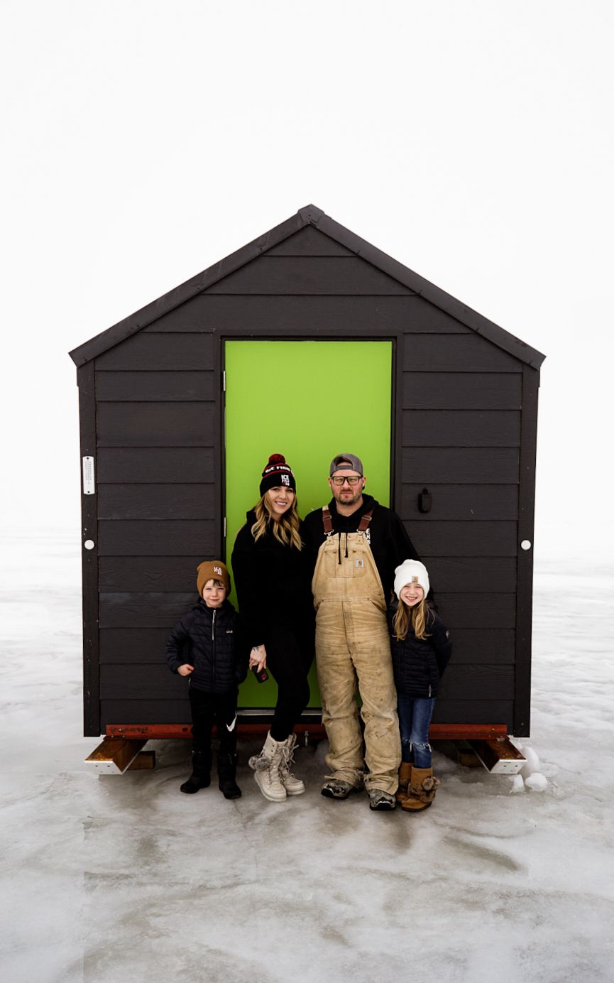 Black ice fishing shelter with bright green door frame on a snowy lake.