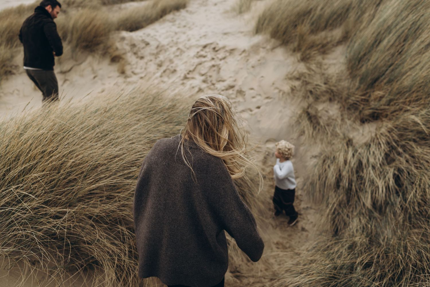 A mother walking down the sandy dune to her son and husband during an outdoor family session with Forever Ours Photography in Kent