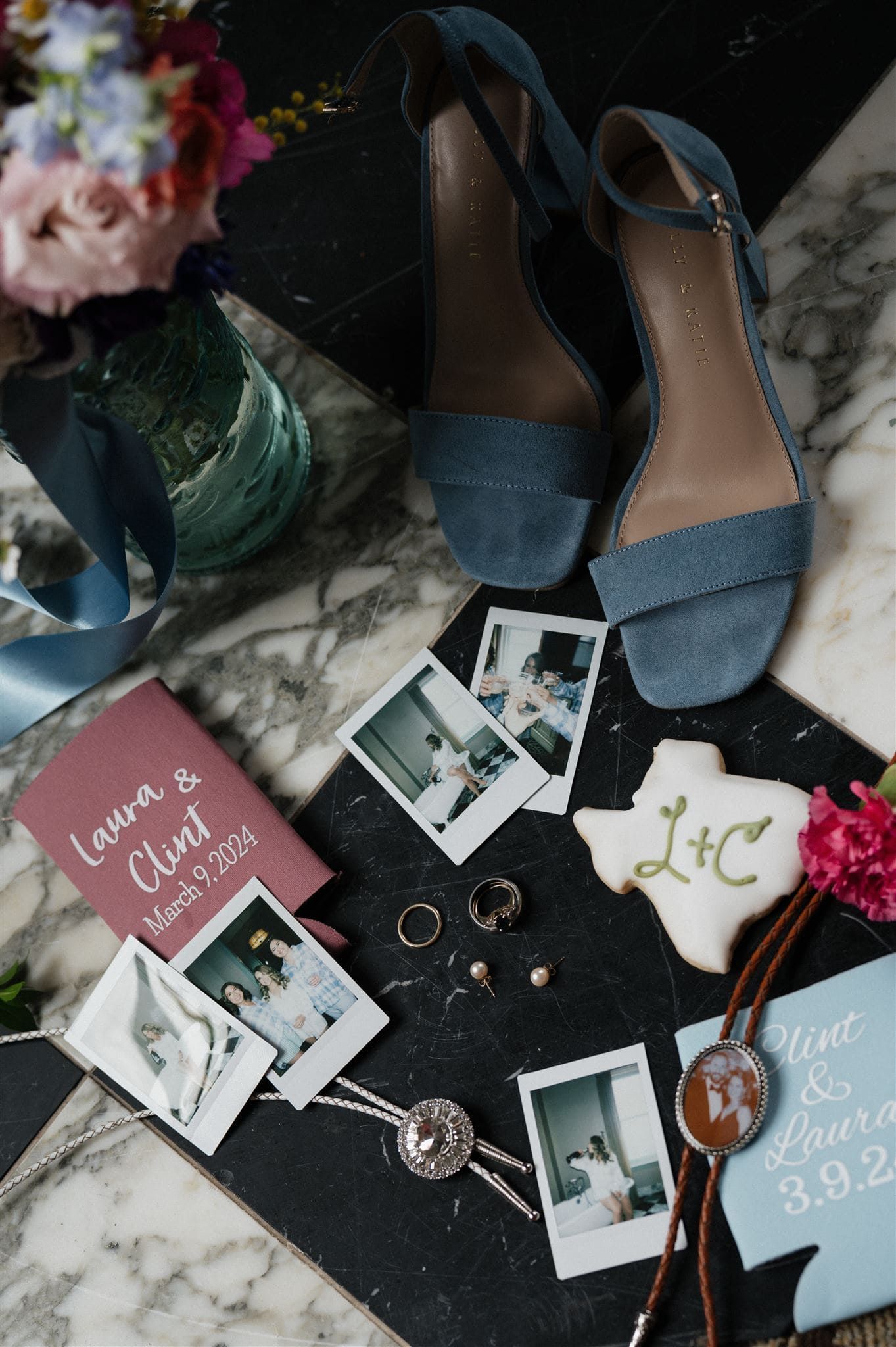 Wedding details including blue sandals, polaroid photos, and decorative items arranged on a marble surface.