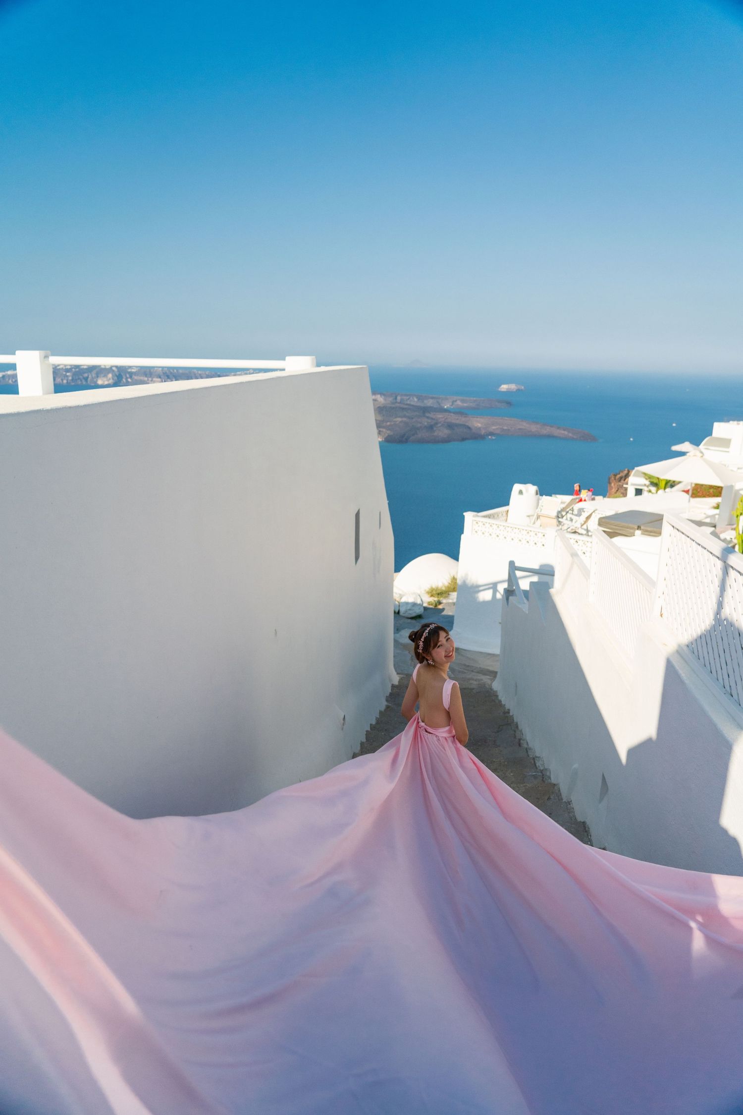 Pink flowing gown against white buildings and Mediterranean Sea views in Santorini.