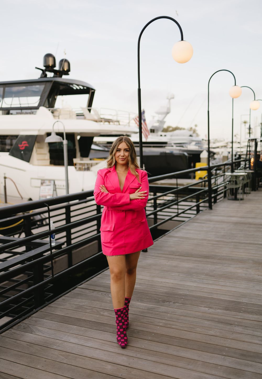 Person in bright pink dress walking along marina boardwalk with boats in background.