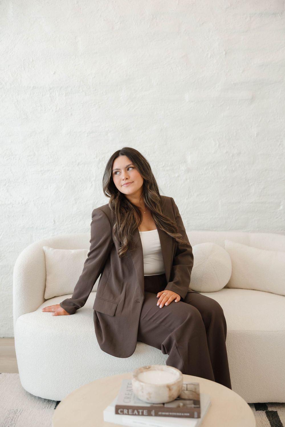 A person wearing a brown business suit relaxes on a curved white sofa with a coffee table in the foreground.