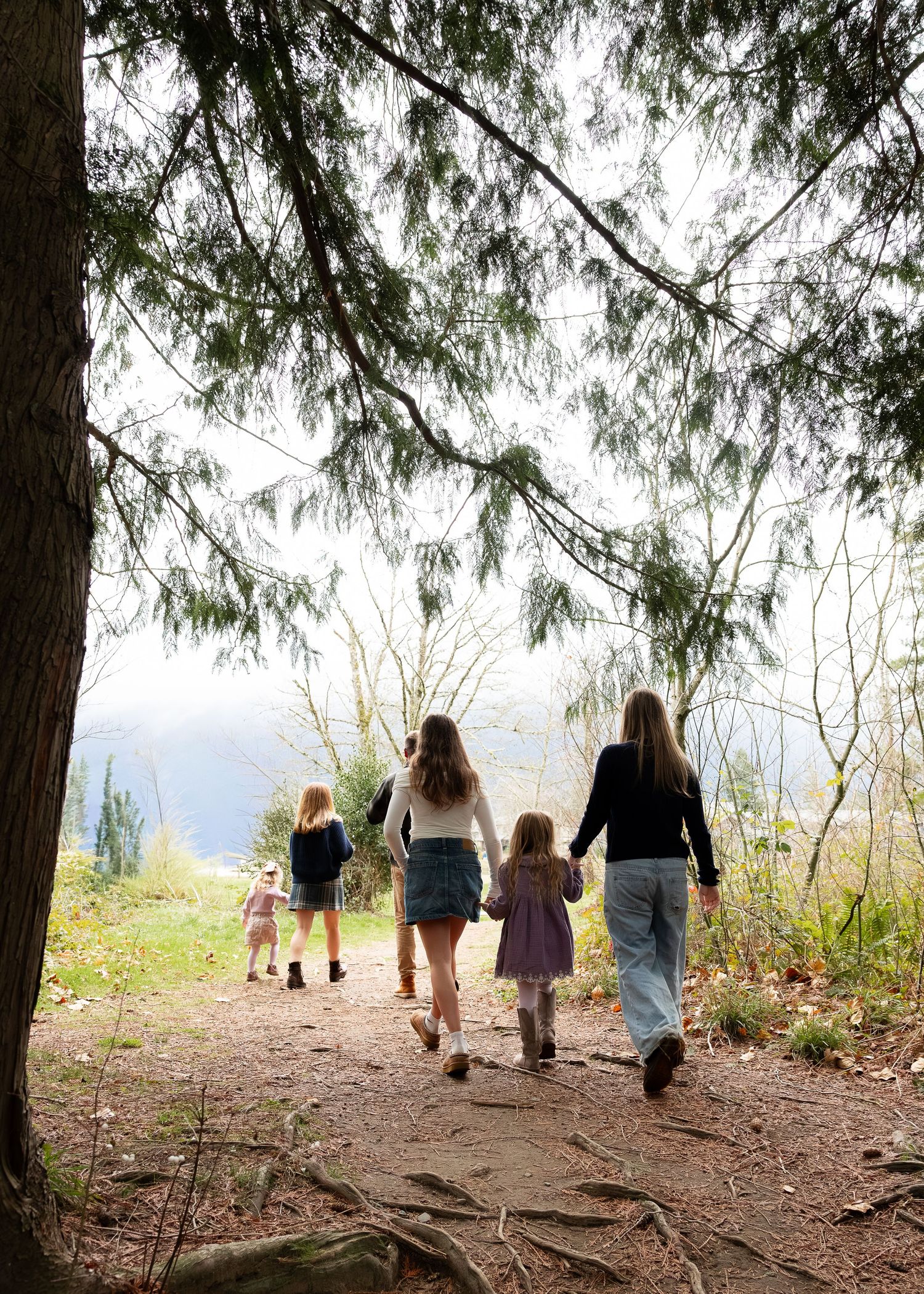 People walk along a forest trail overlooking water on a cloudy day.