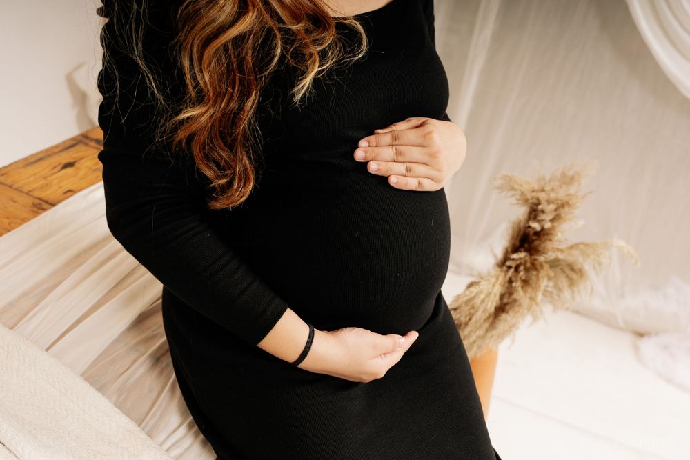 Close-up of pregnant belly in black sweater dress against white backdrop.