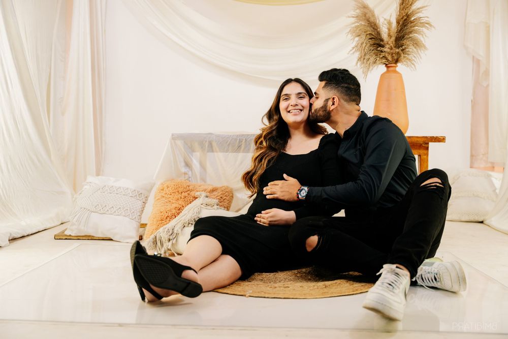 Couple relaxes on round jute rug during indoor maternity photoshoot.