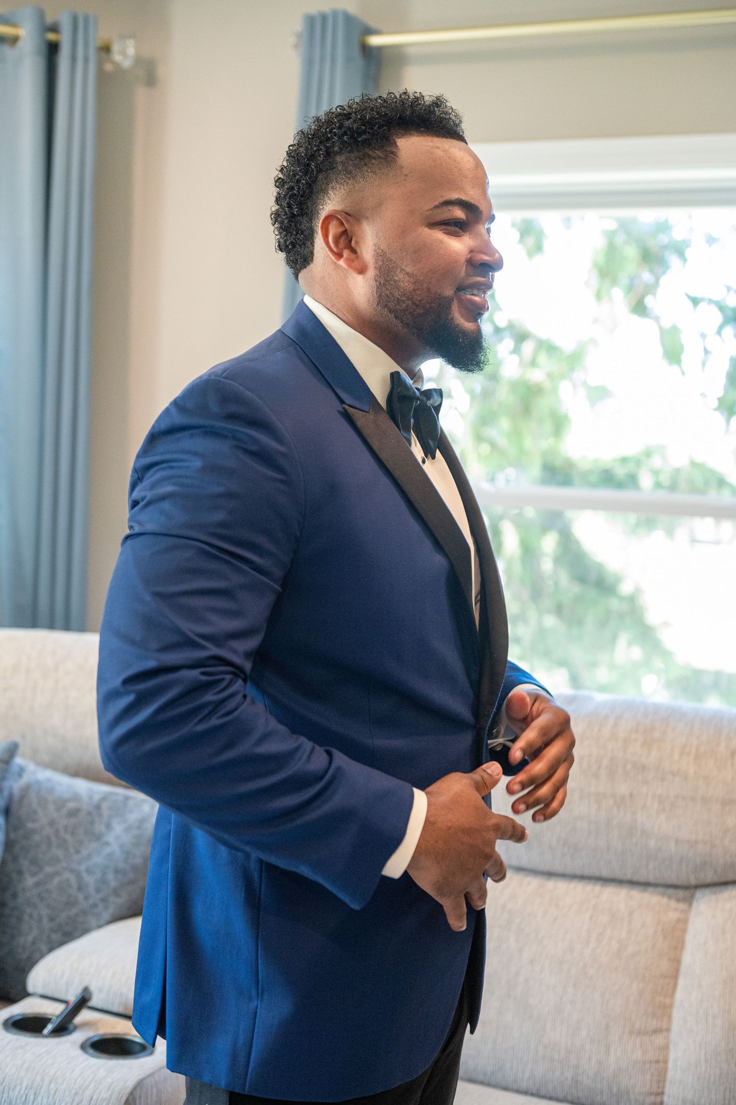 Groom adjusts his navy blue tuxedo jacket while getting ready for wedding.