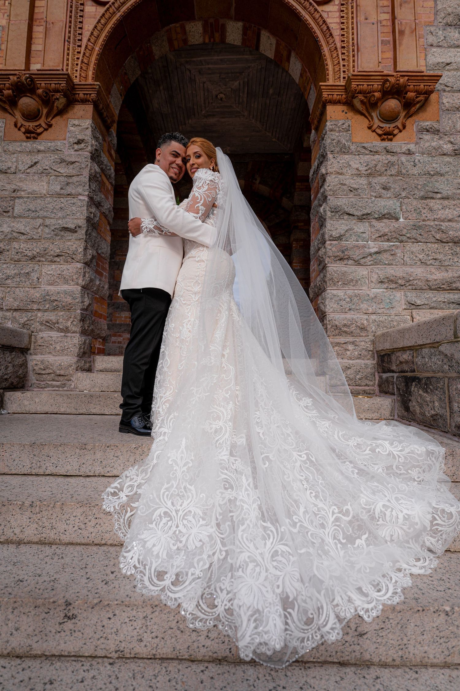 Elegant wedding portrait in front of stone archway with intricate lace dress train.