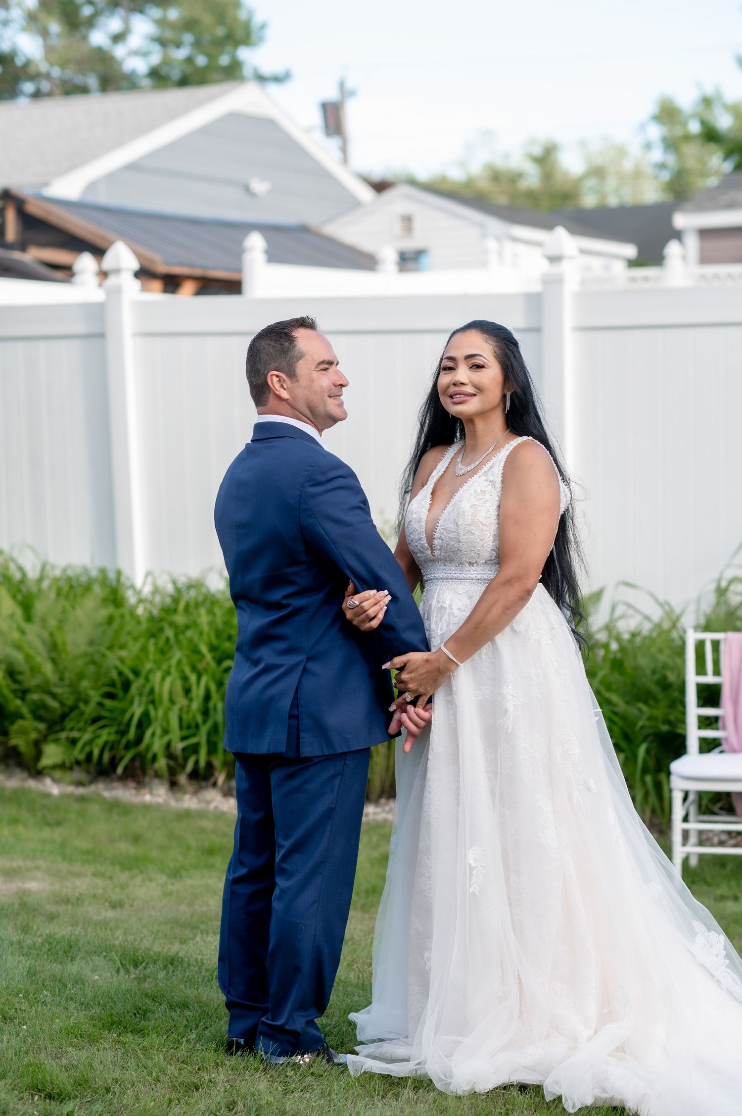 A wedding couple sharing a joyful moment in a backyard garden setting with white fence.