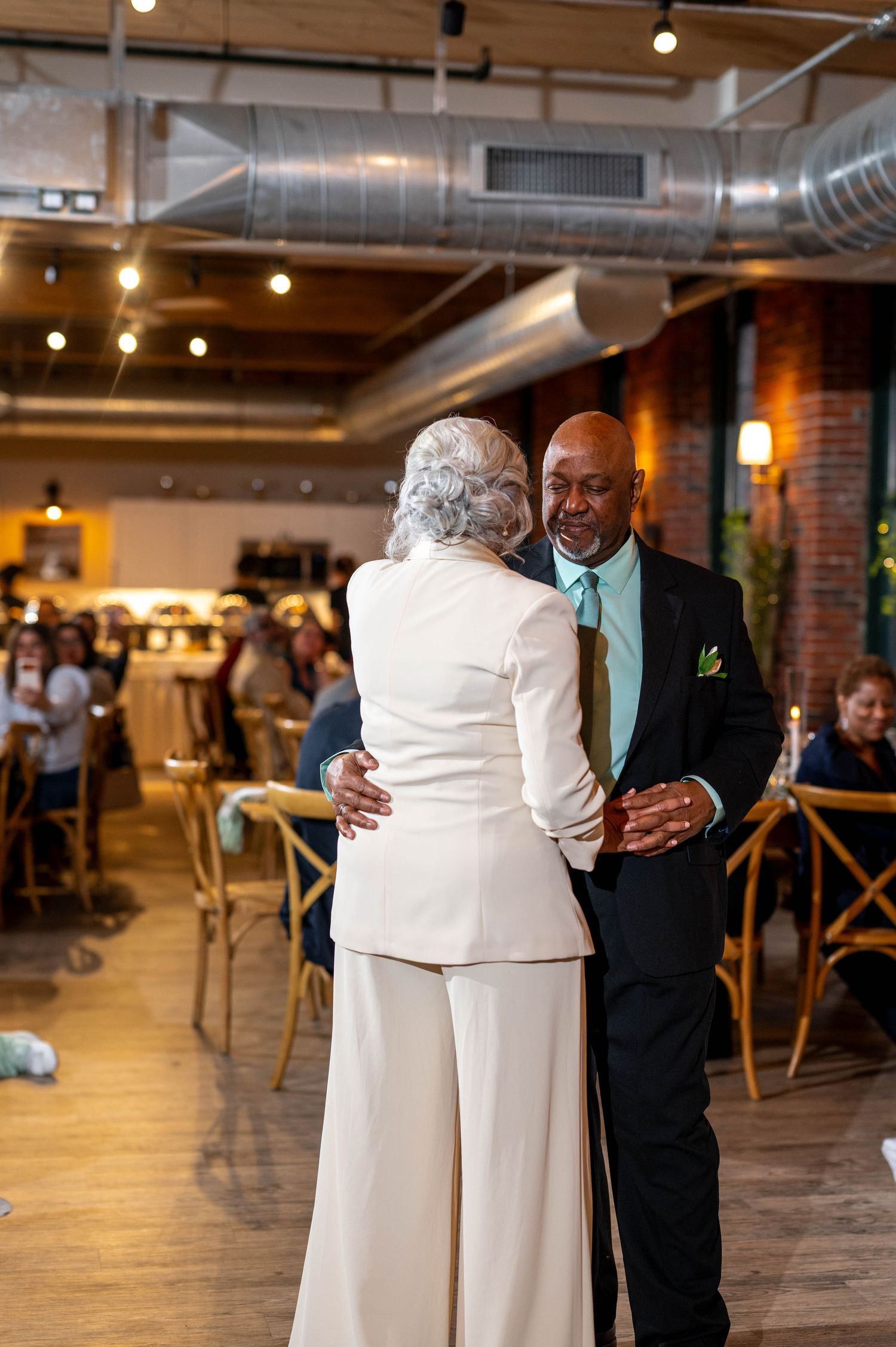 Couple sharing a first dance at a wedding reception in a modern industrial venue with brick walls.
